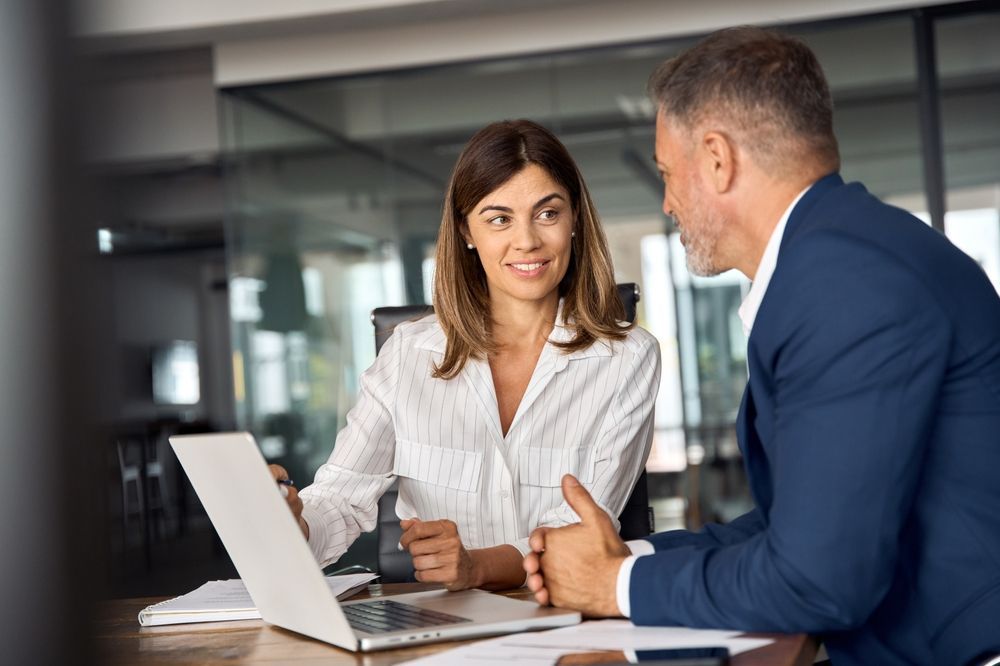 Woman and man in office looking at laptop, discussing.