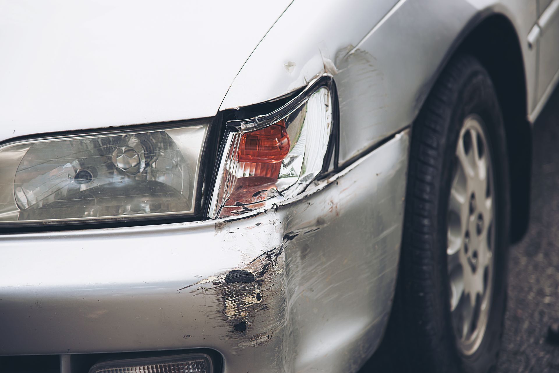 Damaged silver car front end with a cracked headlight and dented bumper after a collision