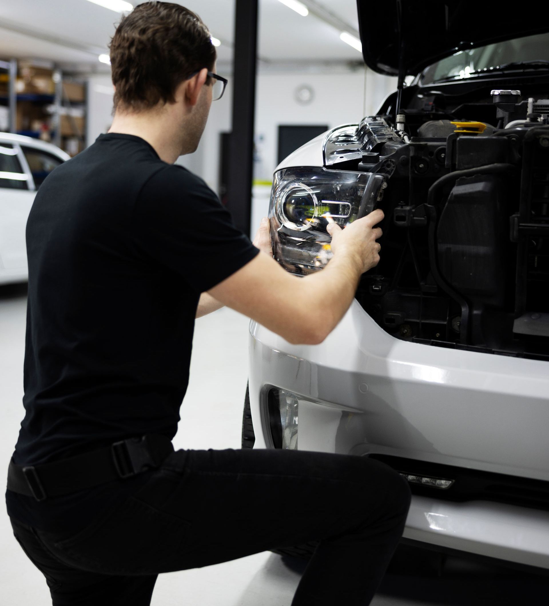 a man is working on the headlight of a car in a garage .