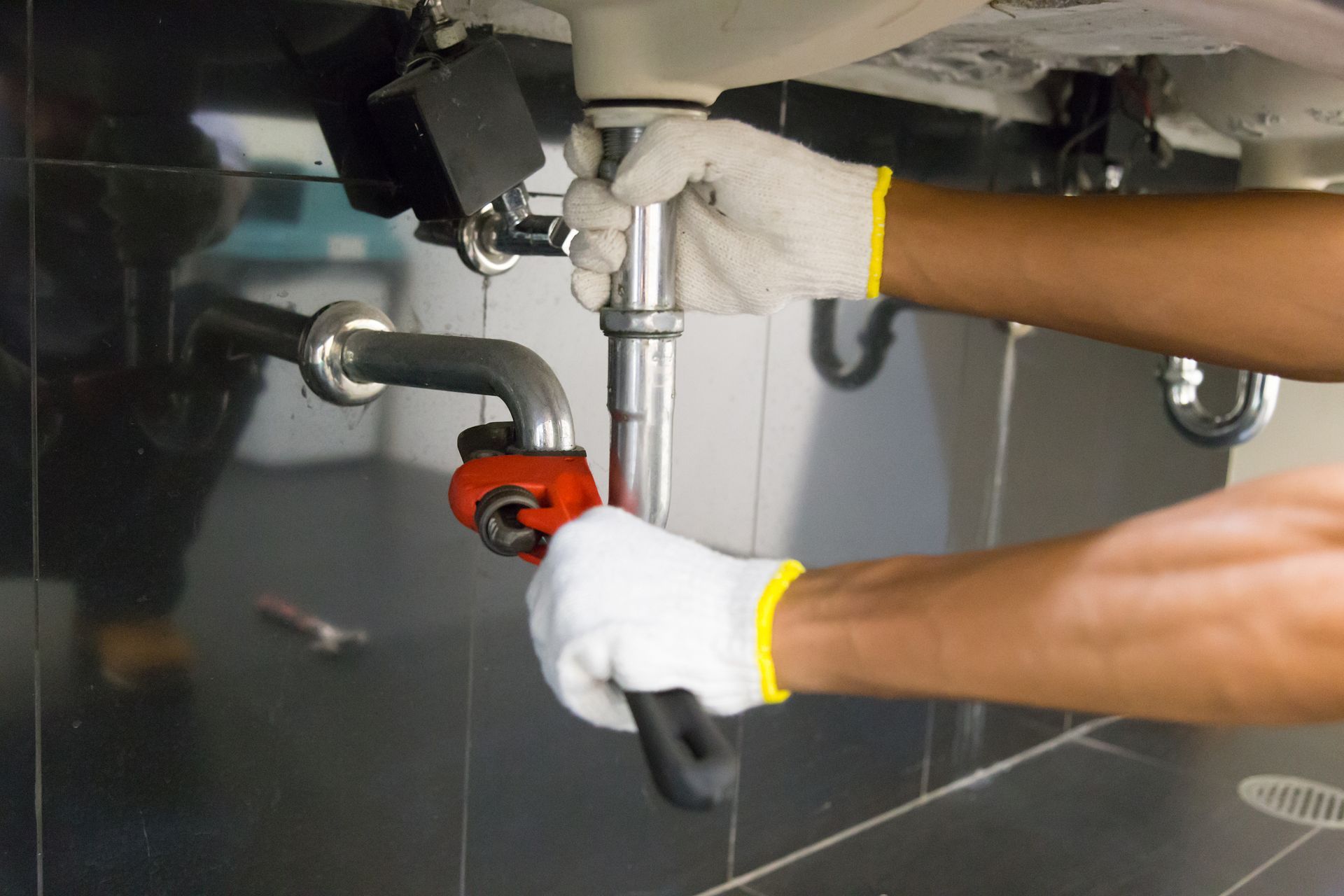 A plumber is fixing a sink with a wrench.