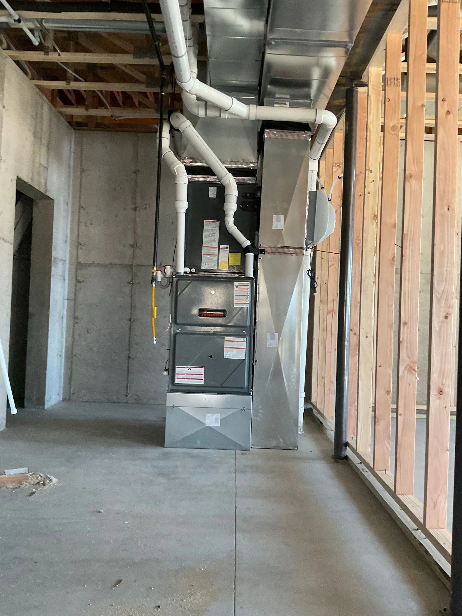 Basement utility room with furnace, exposed ductwork, concrete walls, and open framing.