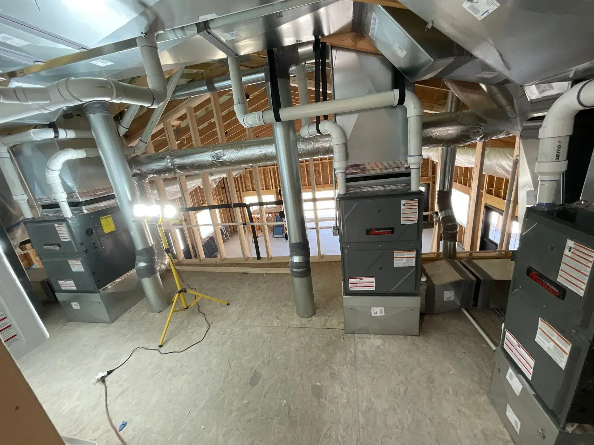 Three HVAC units installed in a new construction attic, with ductwork and exposed framing.