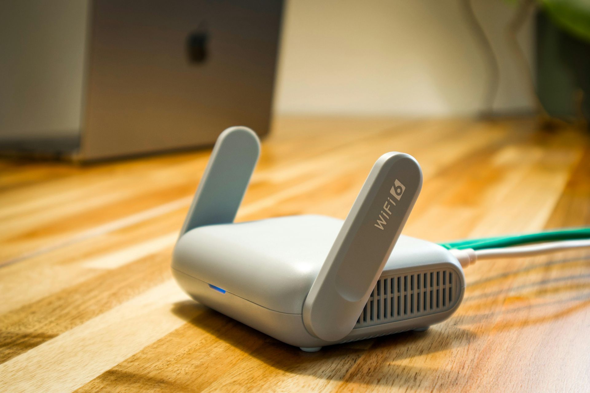 Kleine witte wifi-router met twee rechtopstaande antennes op een houten bureau, met een kabel eraan.