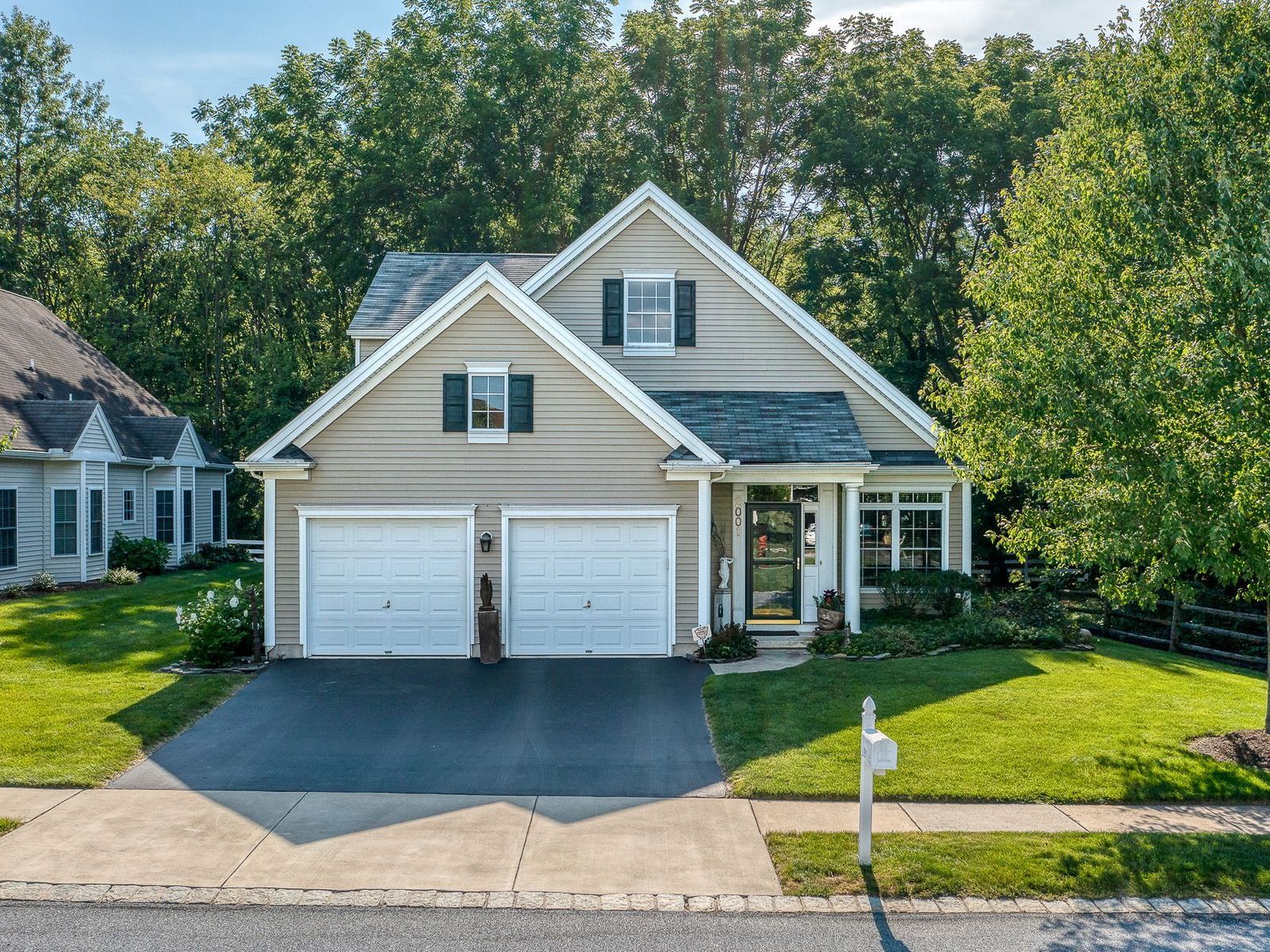 Two-story house with a white garage, green lawn, and trees.
