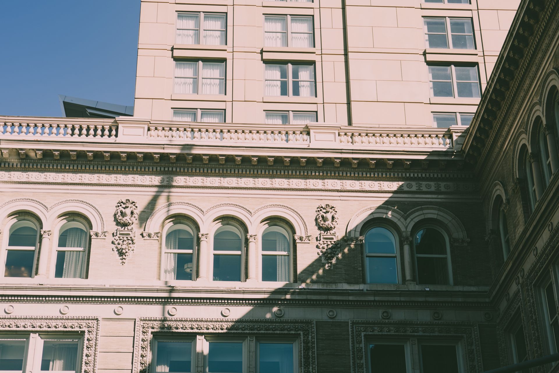 Buildings with arched windows, tan brick facade, and a sunny sky.