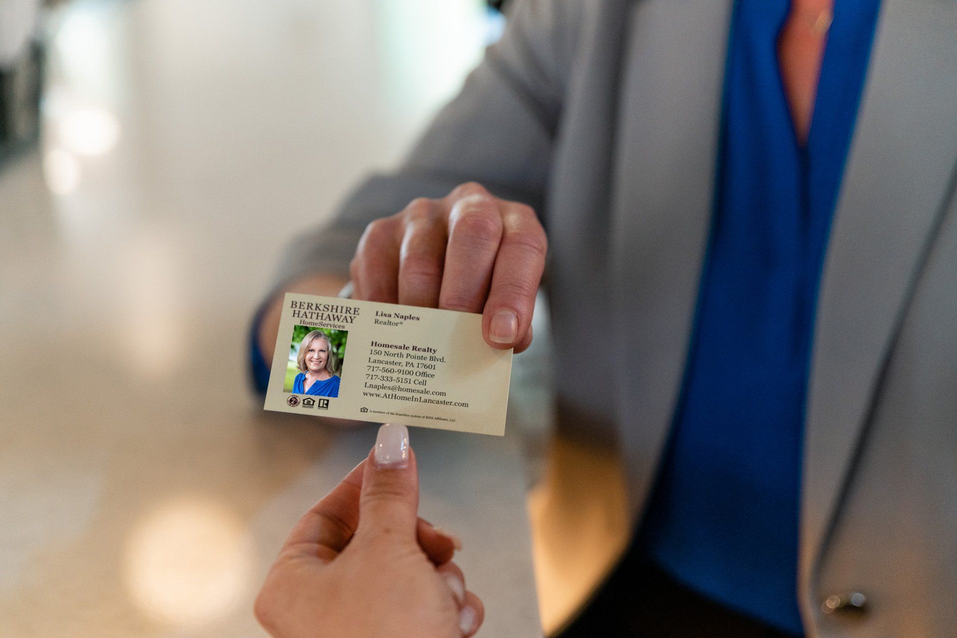 Person handing an ID card to another person. Beige card with a photo, held by a person in a gray jacket.