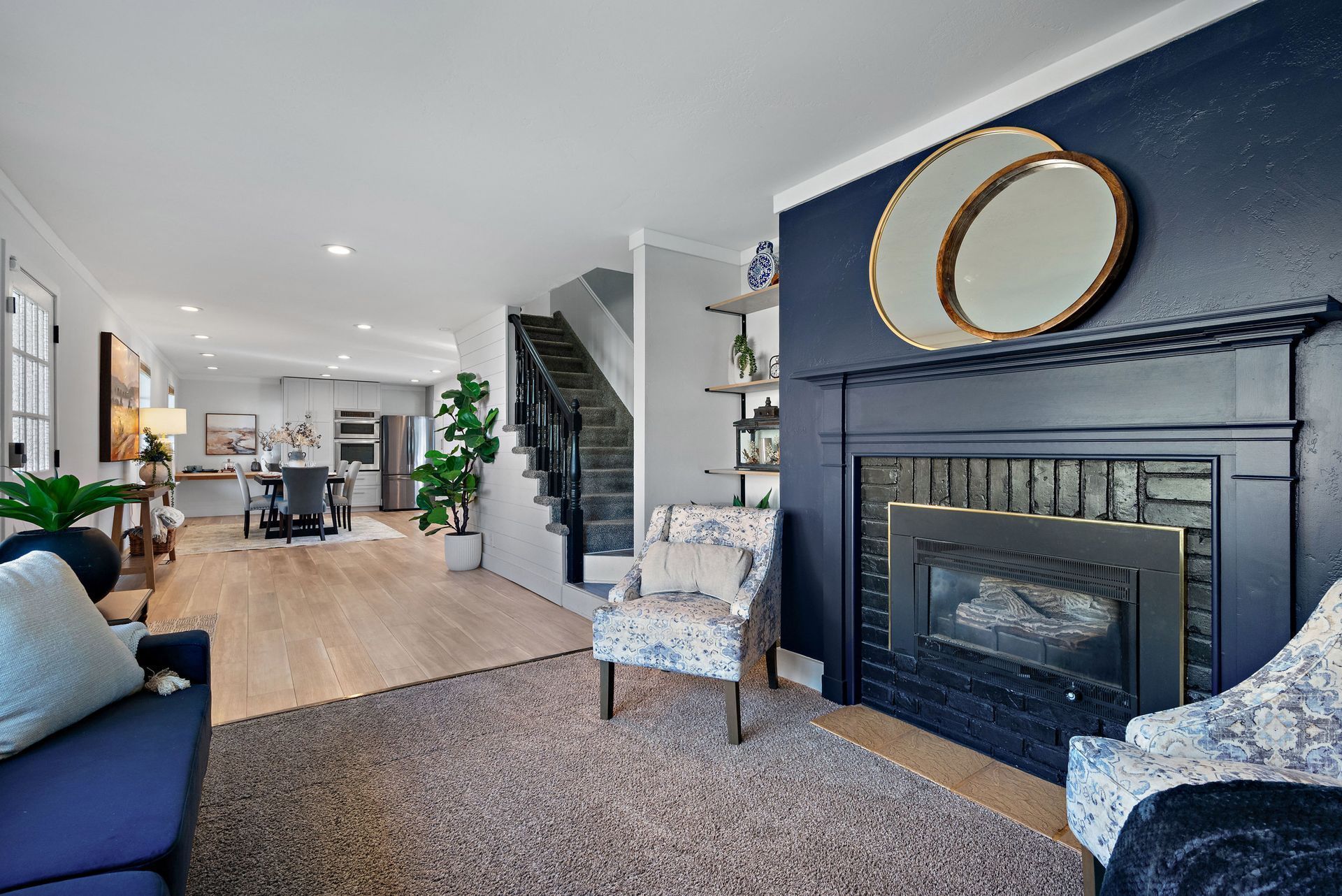 Living room with fireplace, stairs, and open view into a dining area. Blue walls, light wood floors.