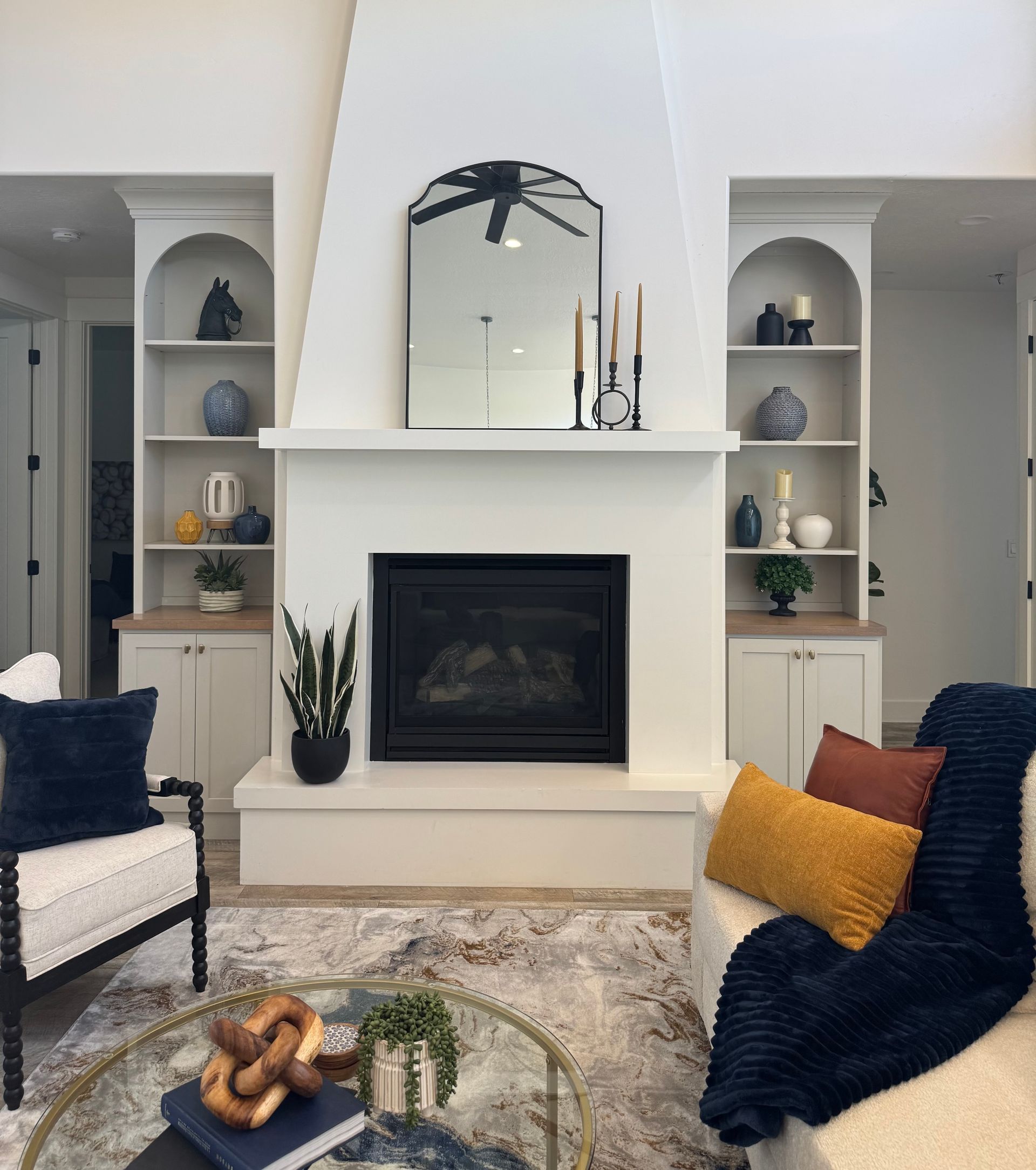 Living room with fireplace, built-in bookshelves, and seating. Furnishings include a round coffee table, and an armchair.