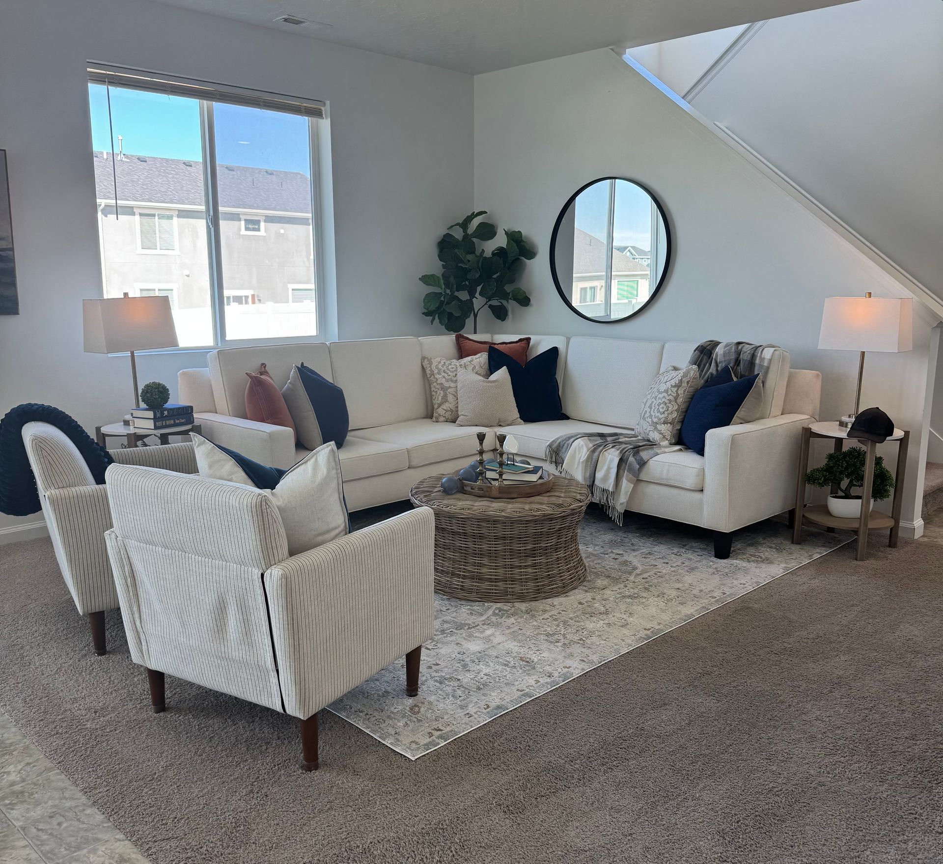 Living room with sectional sofa, armchairs, rug, round mirror, and large window.