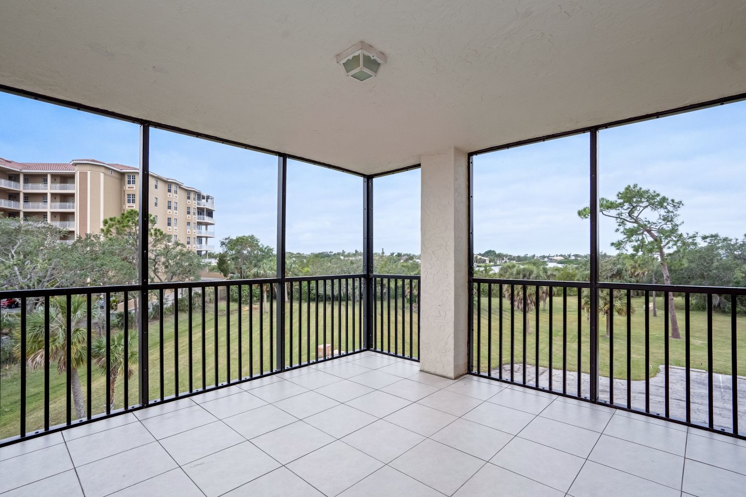 An empty screened in porch with a railing and a view of a field.