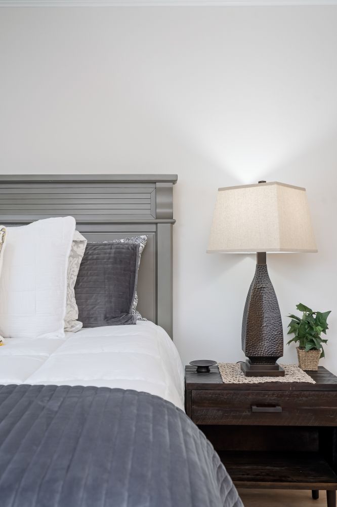 A bedroom with a bed , nightstand , lamp and plant.