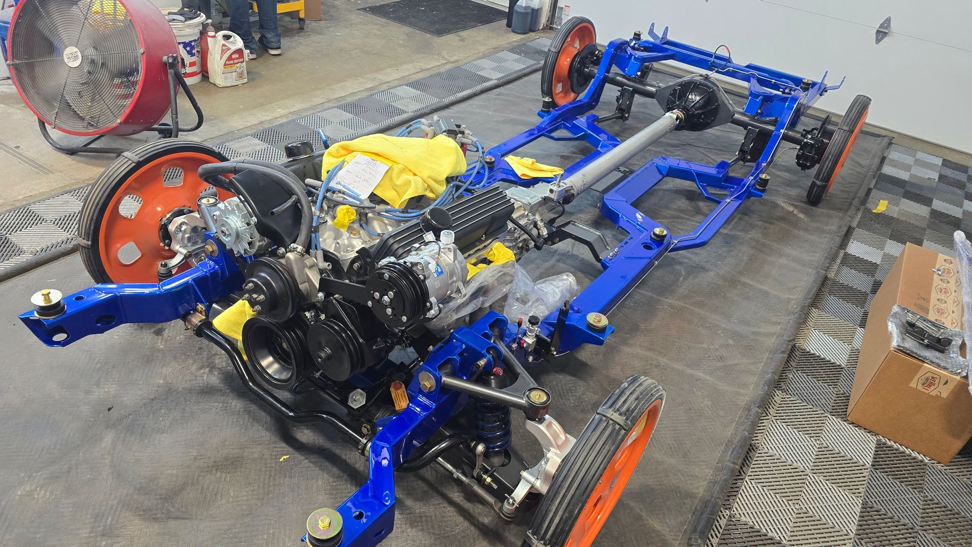 Blue car chassis with engine and orange wheels in a workshop, viewed from above