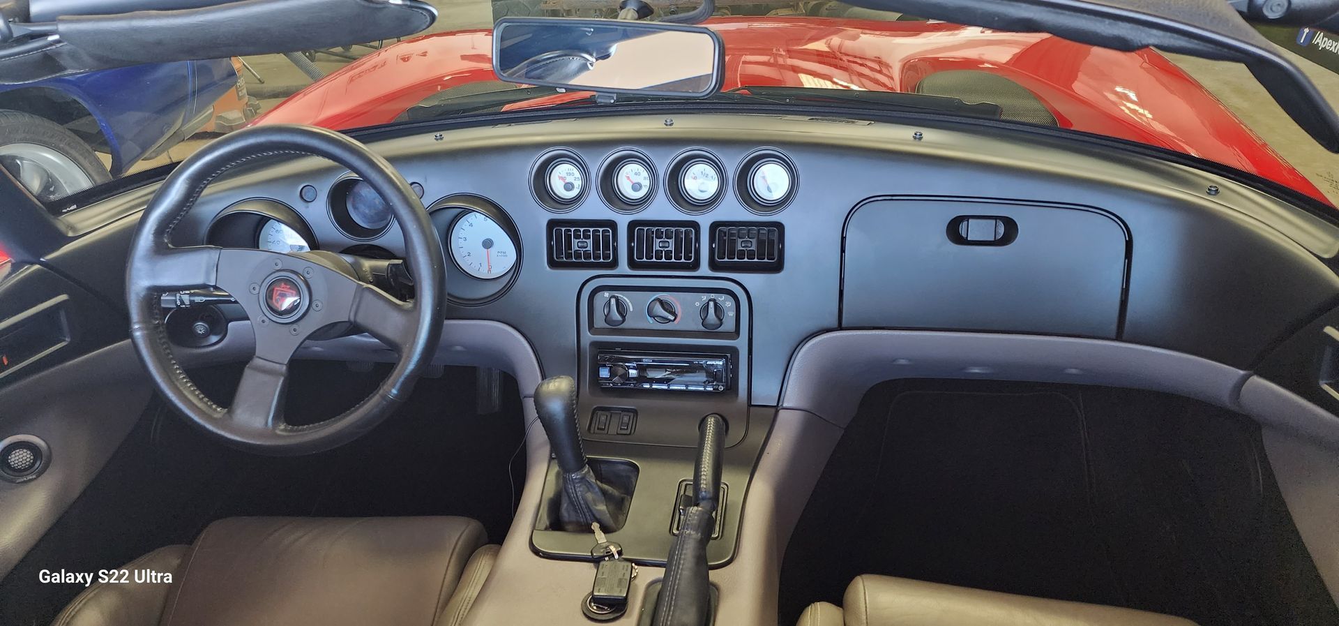 Dodge Viper dashboard with gauges, steering wheel, radio, and gear shift. Brown seats and a red exterior are visible.