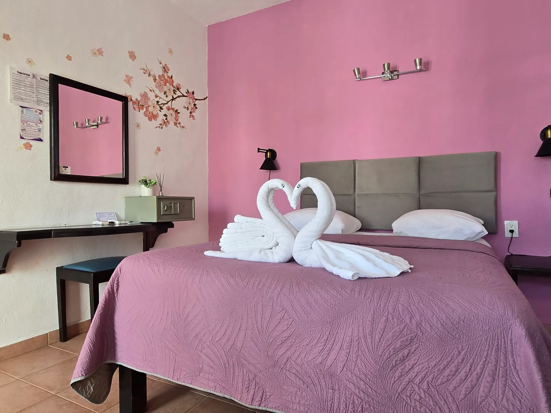 Habitación rosa con un cuadro de cisnes hecho con toallas sobre la cama y un espejo de tocador en la pared.