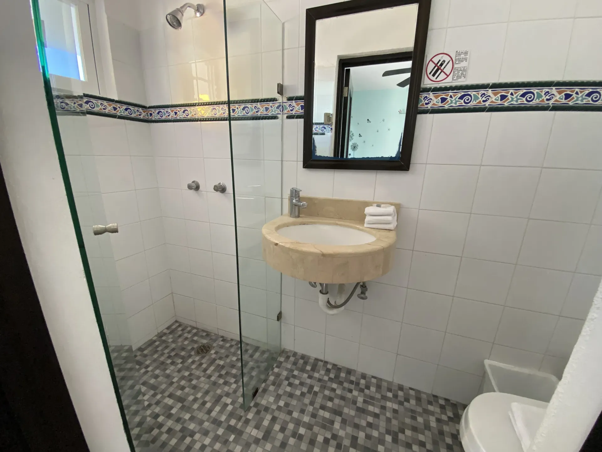 Baño pequeño con azulejos, ducha de cristal, lavabo, espejo e inodoro.