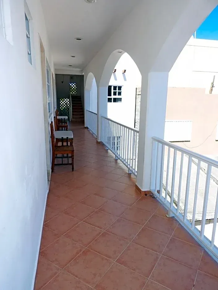 Pasillo cubierto con baldosas, arcos blancos, barandilla y sillas a lo largo de la pared.