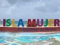 Tres personas en bicicletas, cascos y mochilas están de pie en un muelle, con vistas a una bahía con barcos .