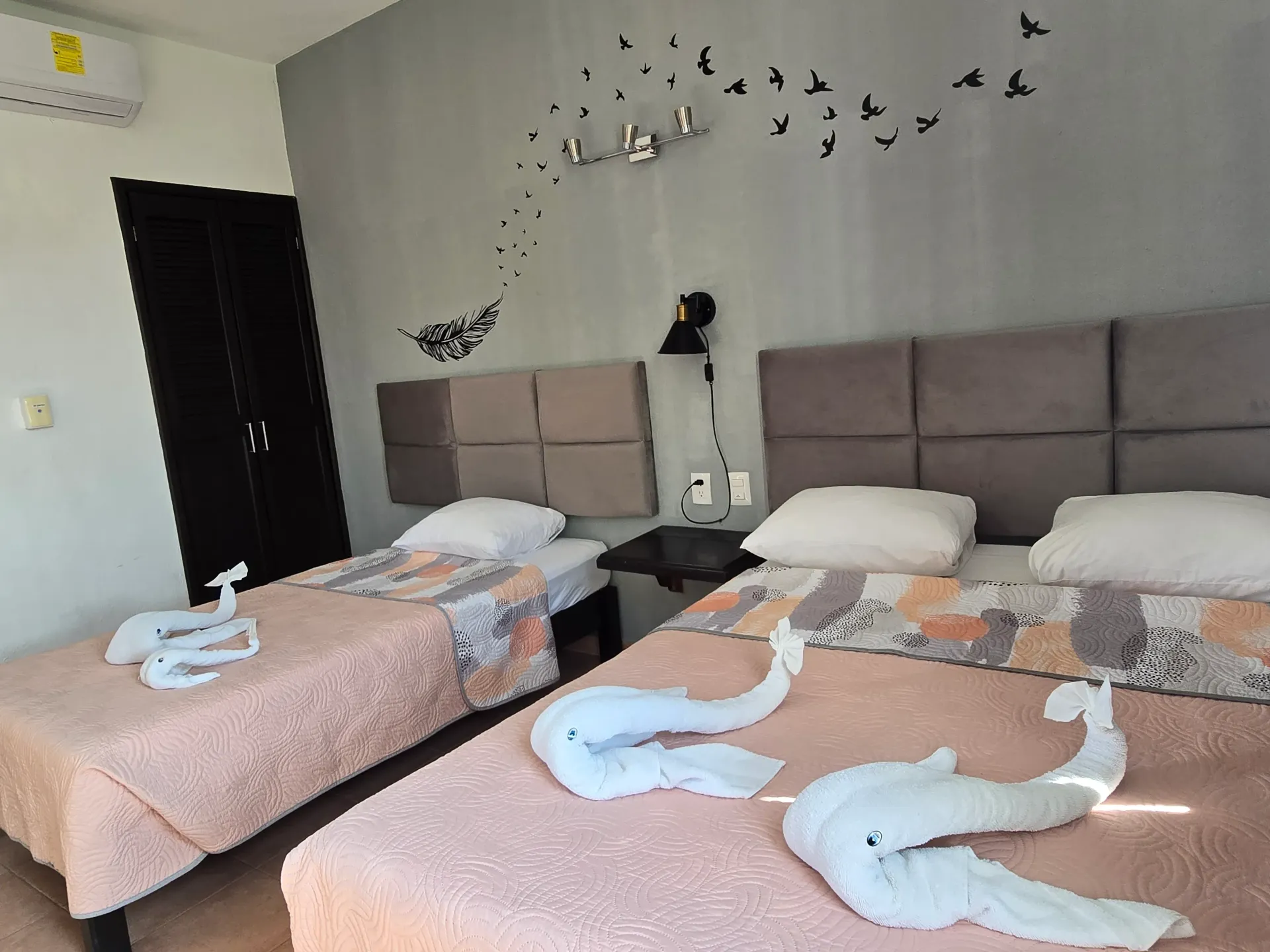 Habitación con dos camas, cabeceros grises, decoración de mariposas en la pared y cisnes hechos con toallas.