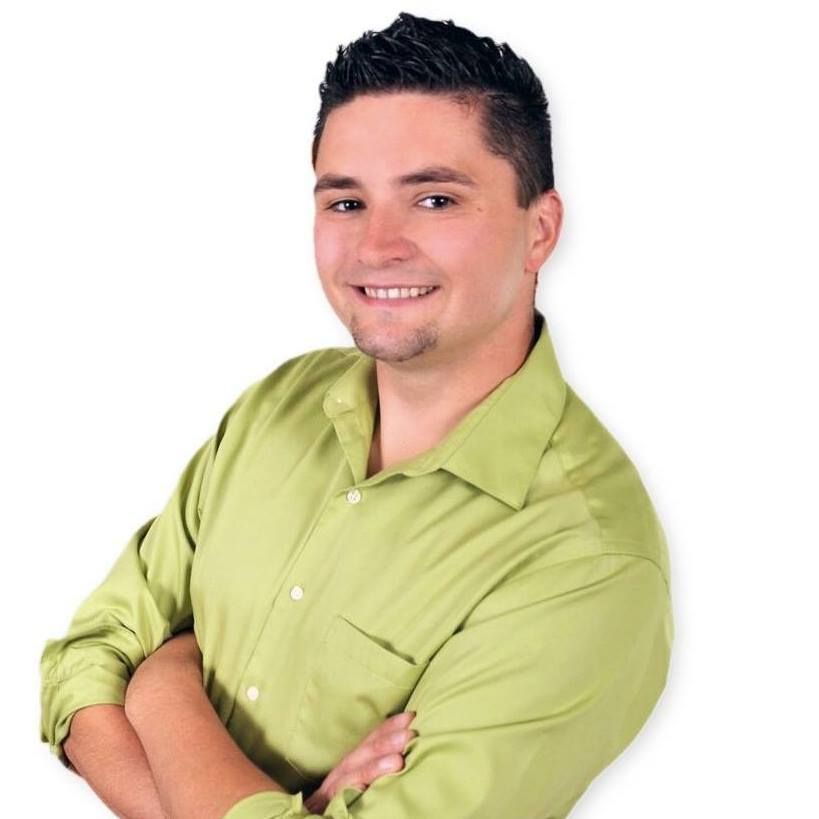Man in a green shirt smiles, arms crossed, against a white background.