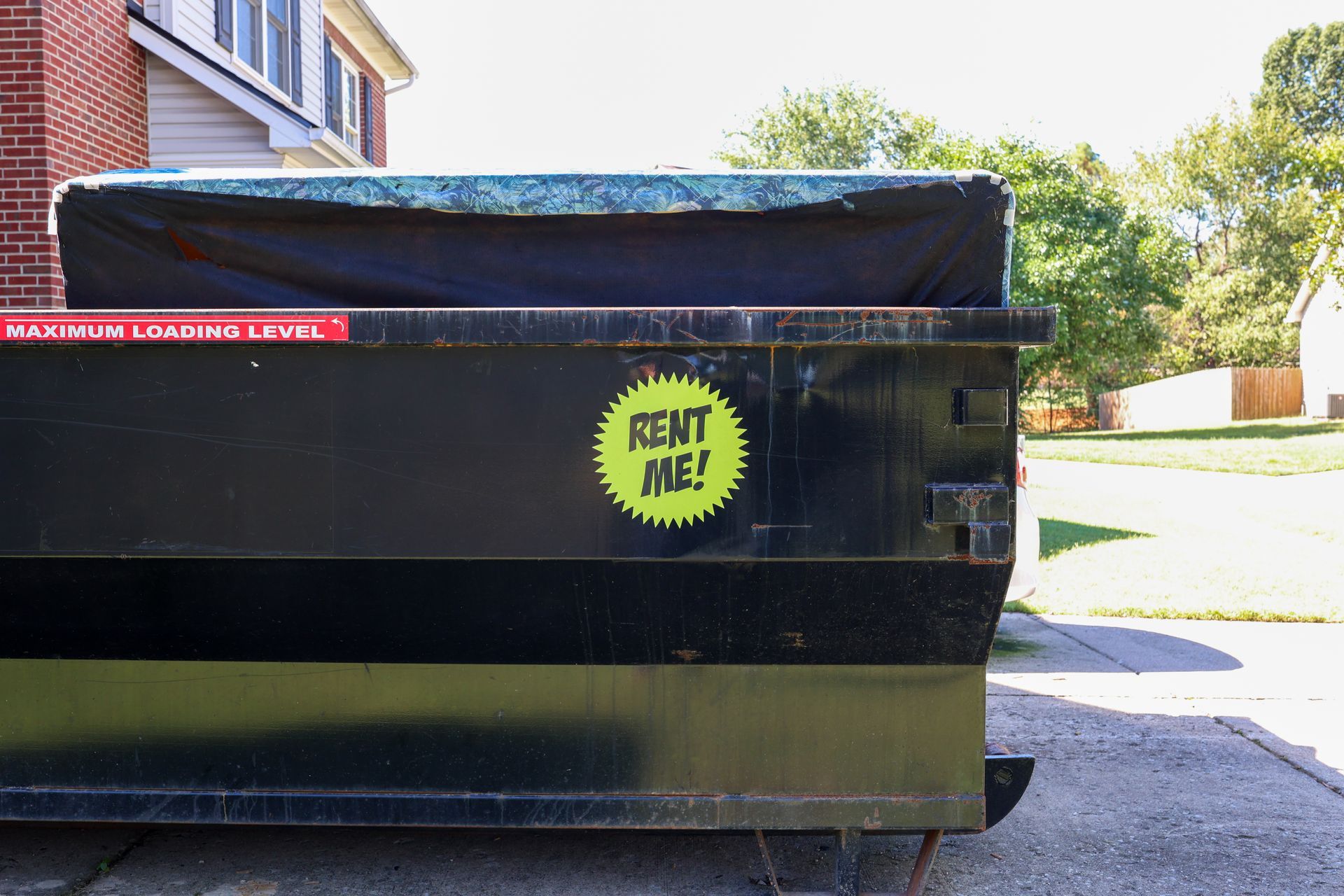 A black roll-off dumpster loaded near capacity with a tarp cover in a residential driveway