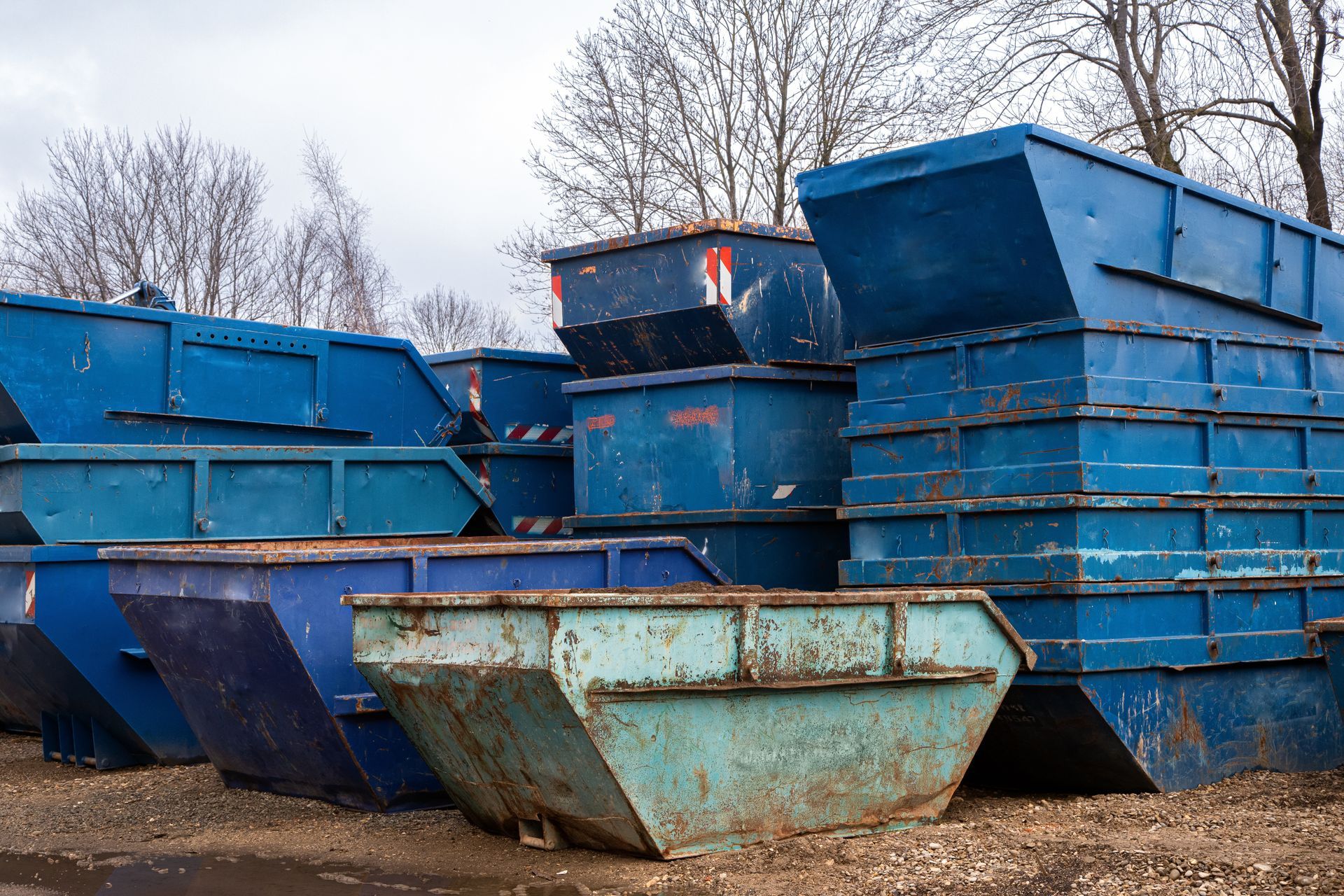 Stack of large blue metal dumpsters arranged outdoors on a dirt lot.