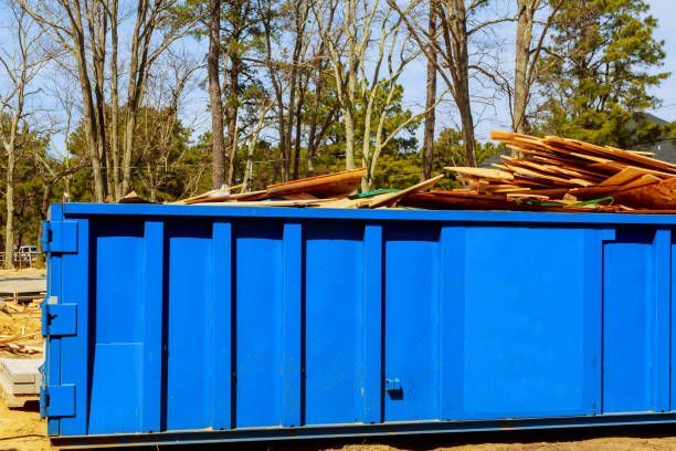 A blue dumpster filled with wood is sitting on top of a dirt field.