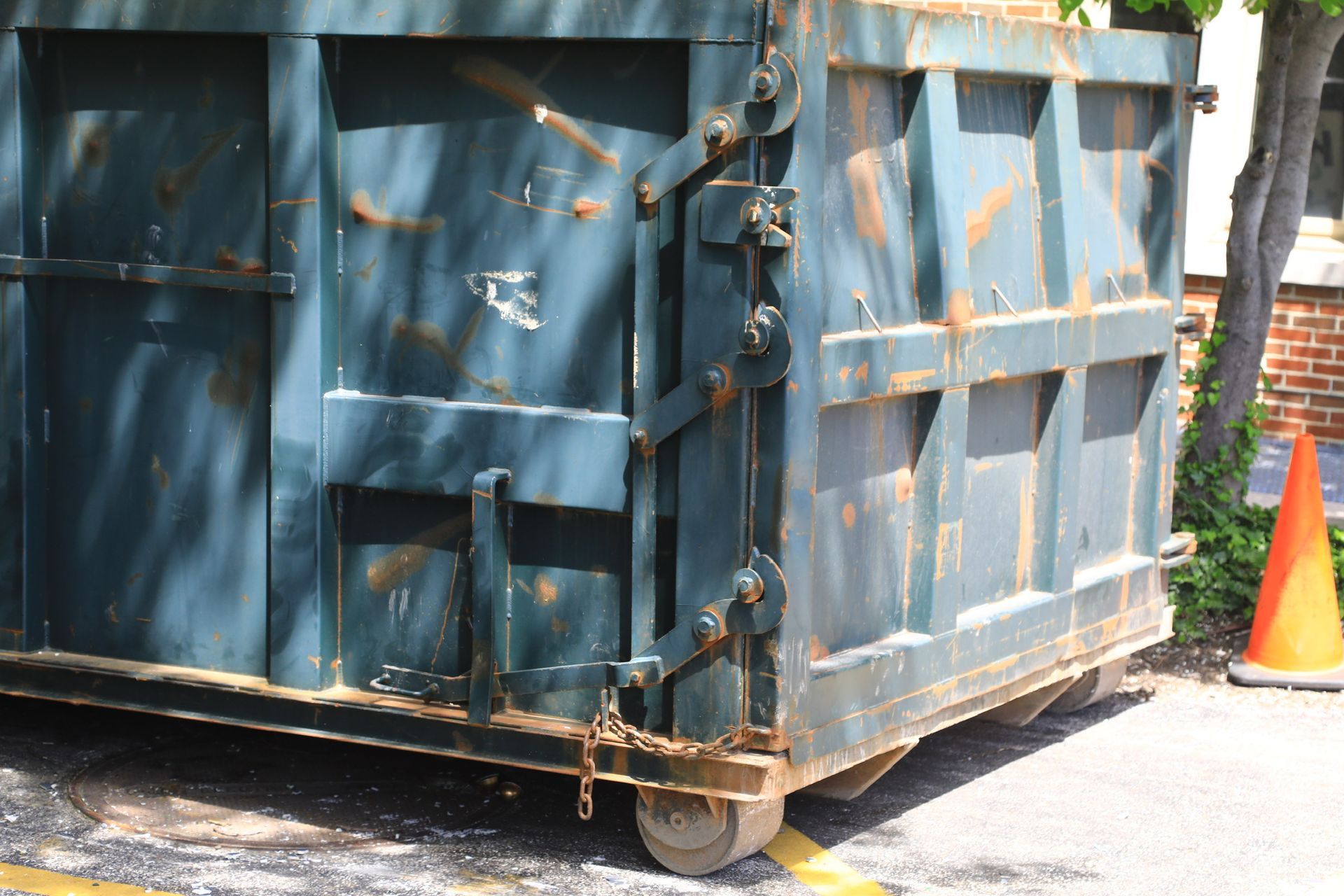 A blue dumpster is parked in a parking lot next to an orange cone