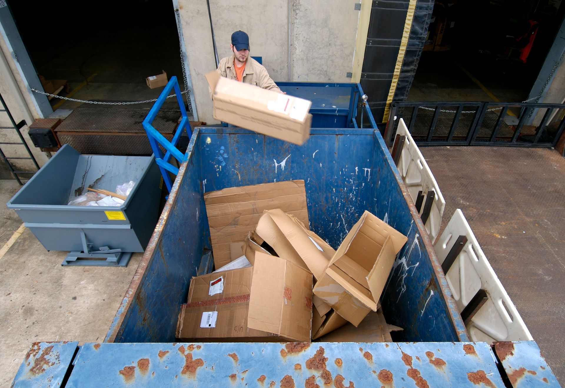 A man is throwing a cardboard box into a dumpster