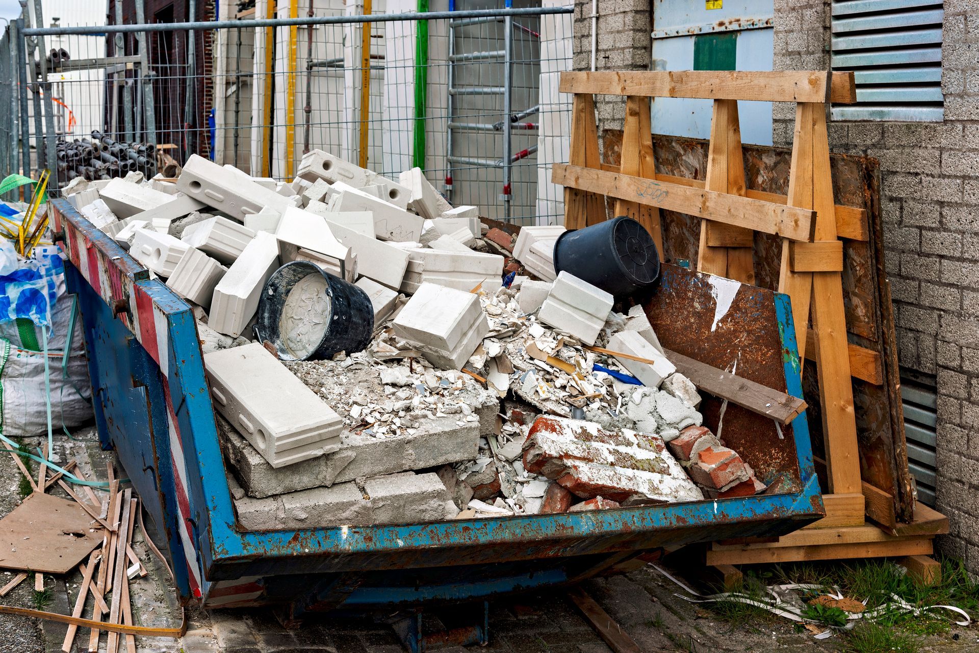 A dumpster filled with bricks is parked in front of a building under construction.