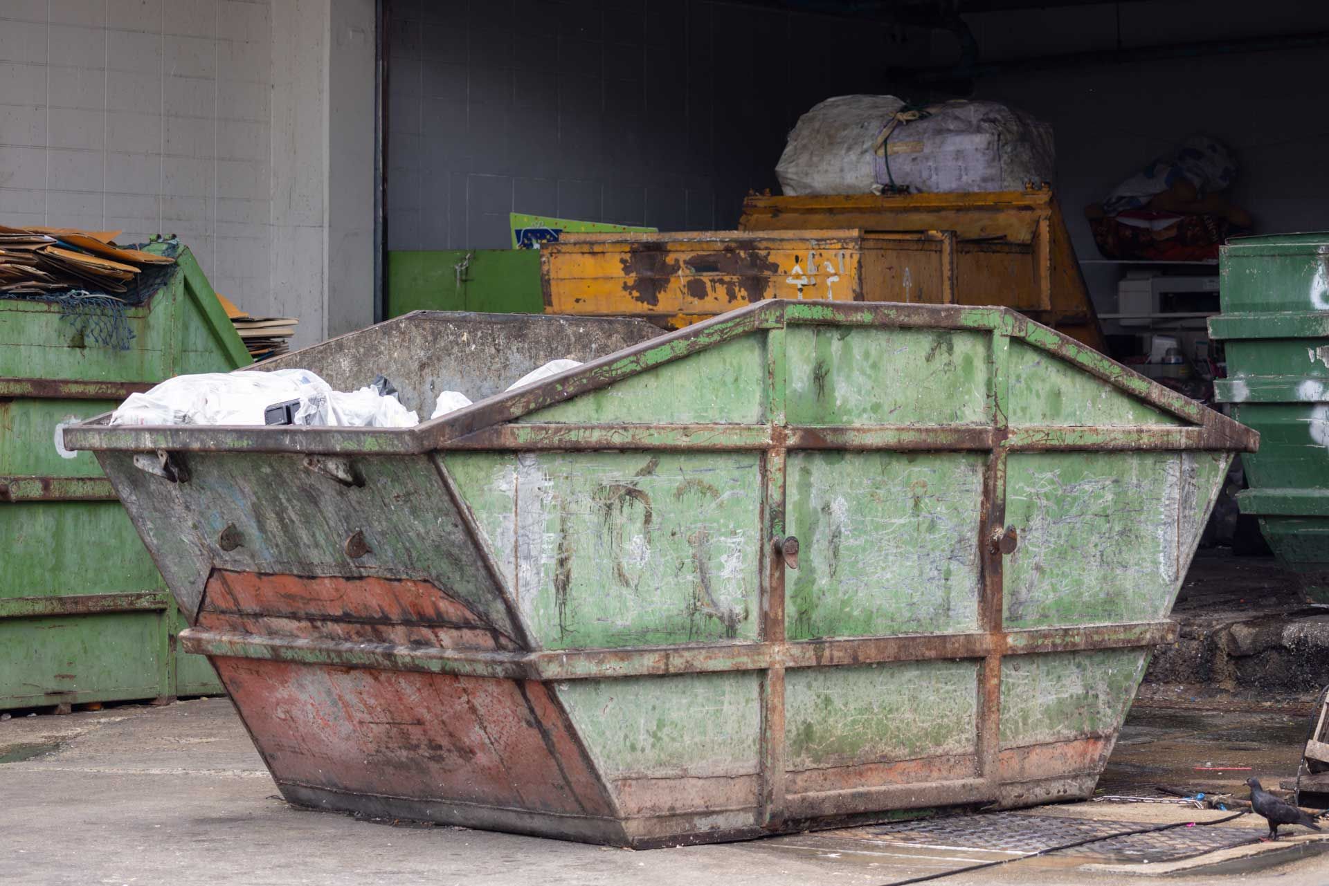 A green dumpster with a red lid sits in a lot. A green dumpster with a red lid sits in a lot.