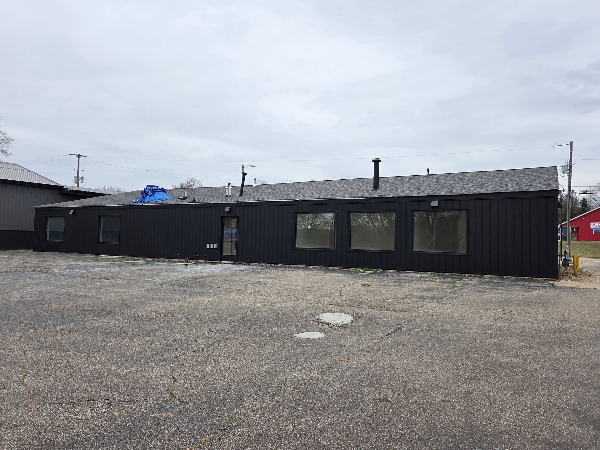 Black single-story building on a gravel lot under a cloudy sky