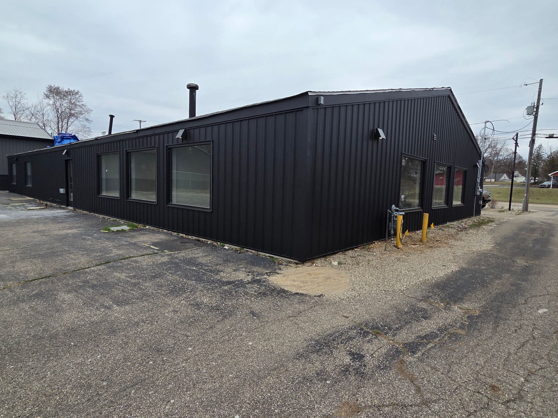 Black corrugated metal building on a gravel lot under an overcast sky