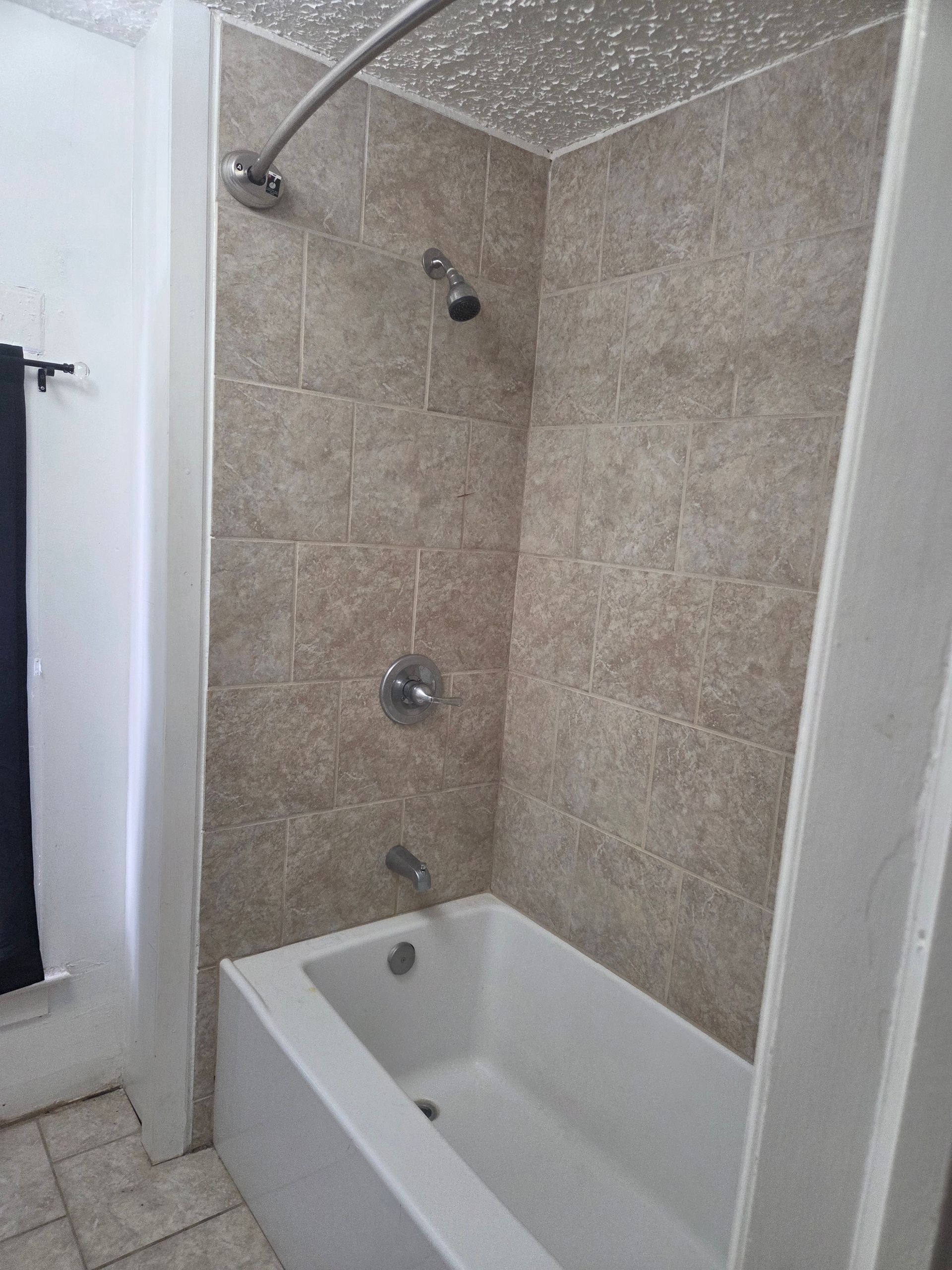 Small tiled bathroom shower over a white bathtub with a showerhead and curtain rod