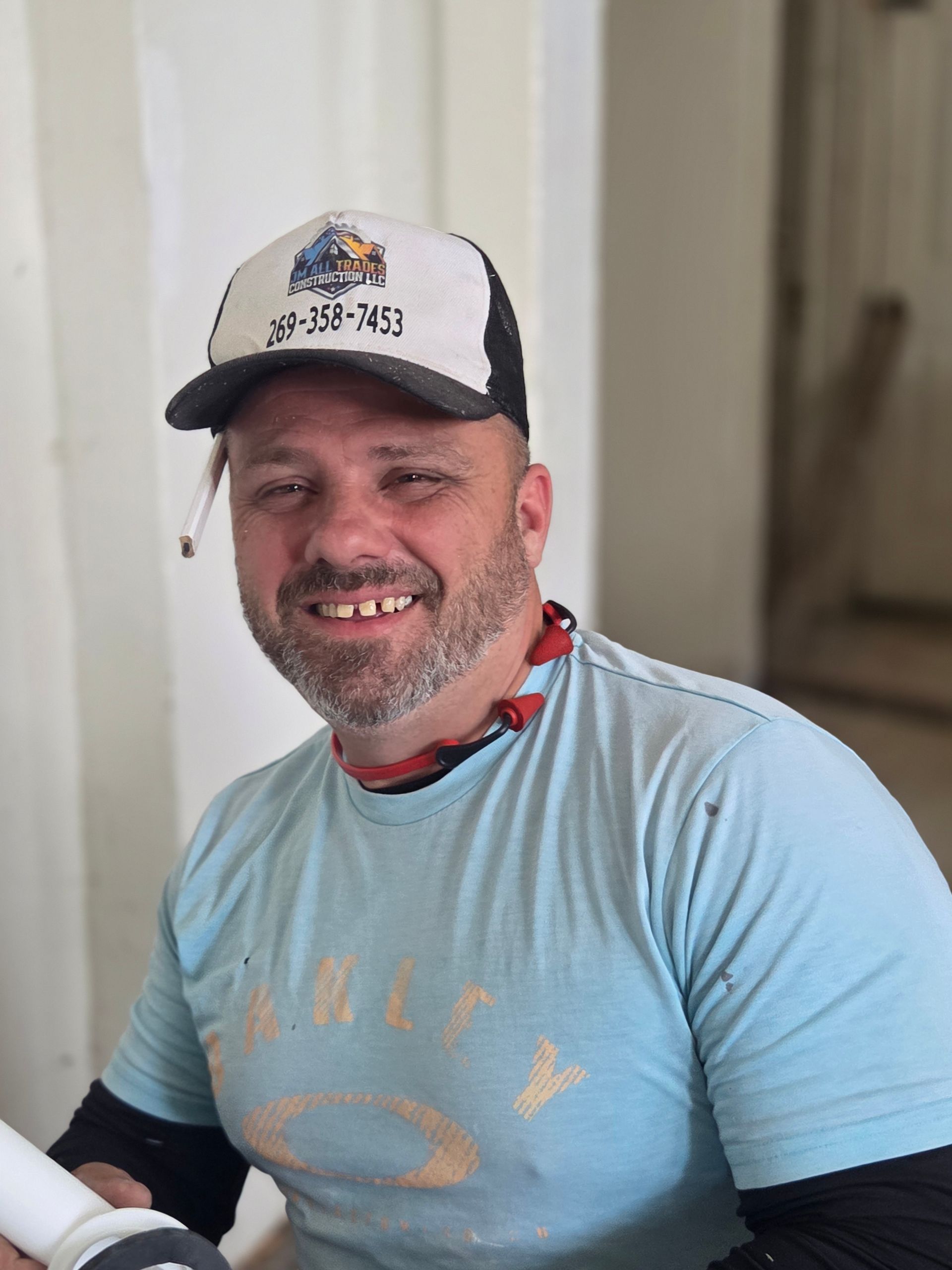 Smiling man in a white cap and light blue T-shirt sitting indoors holding a white object