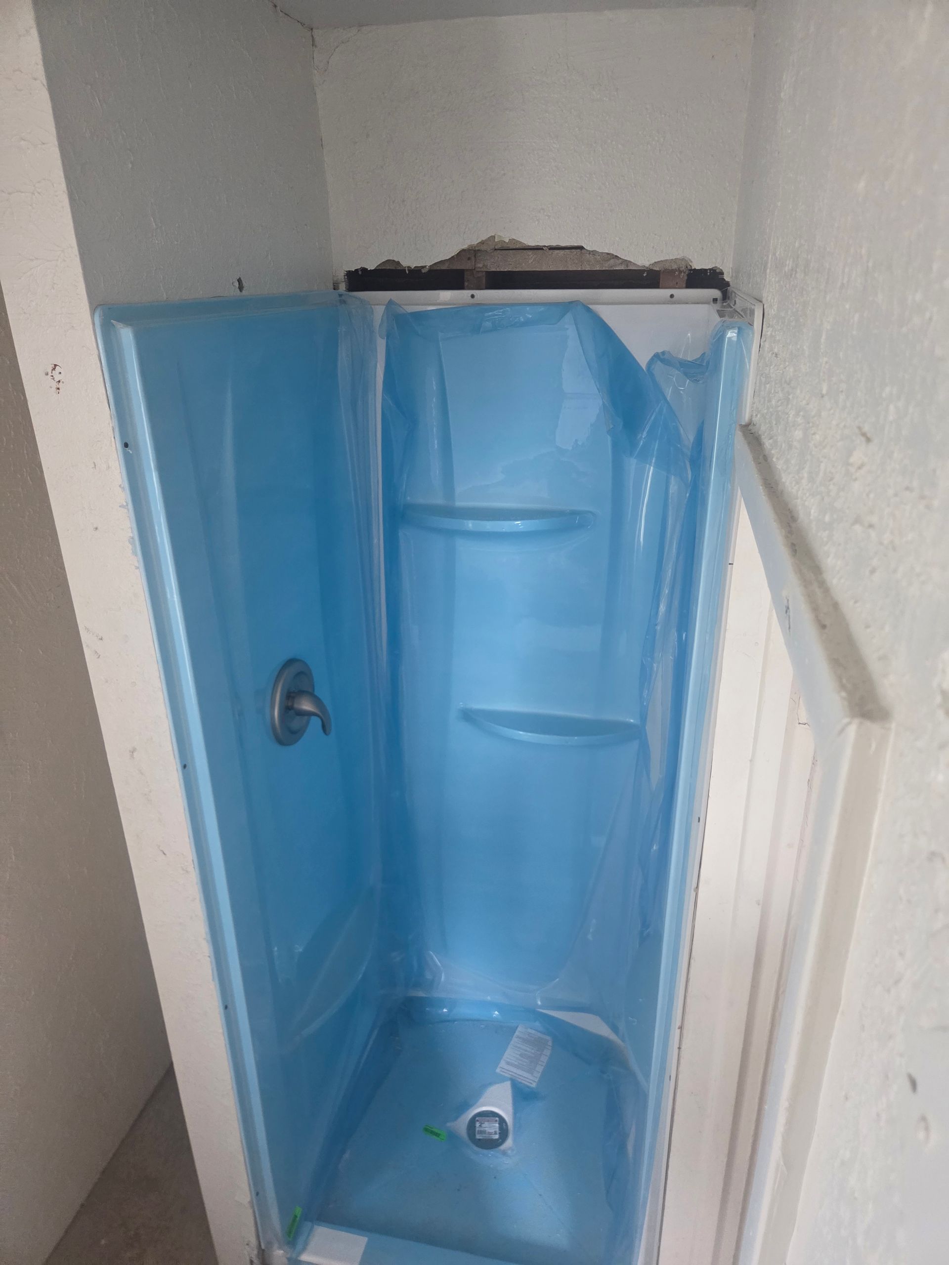 Blue shower stall with built-in shelves and a showerhead, seen from the bathroom doorway