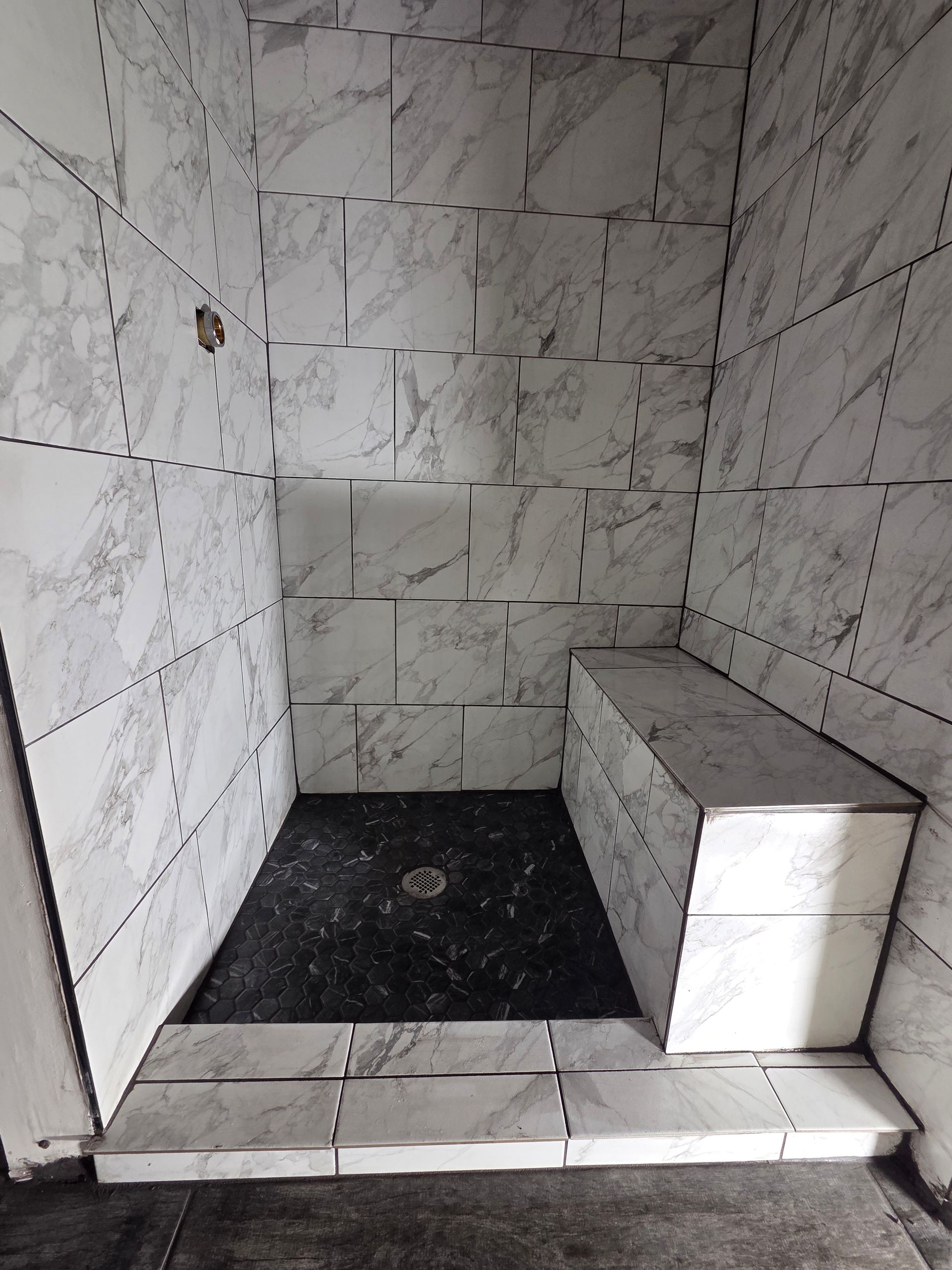 Small tiled shower stall with white marble walls, black floor, and a built-in bench on the right.