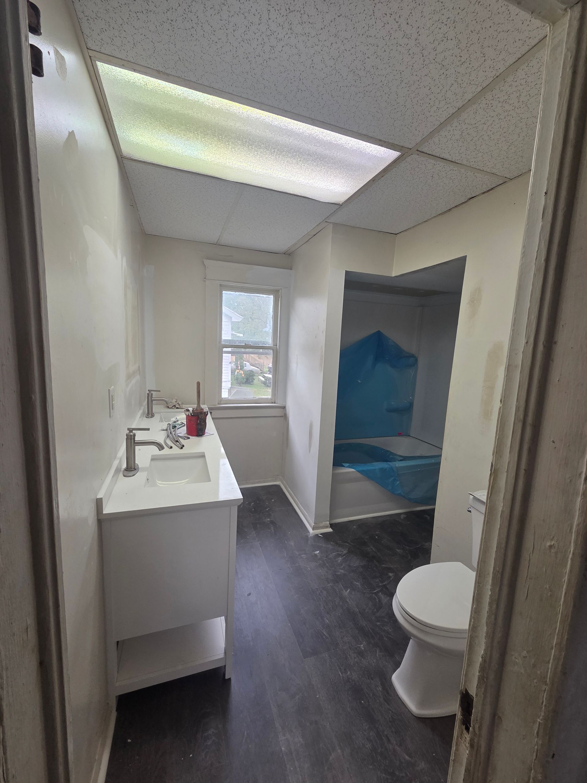 Small bathroom with white sink, toilet, window, and blue shower curtain.