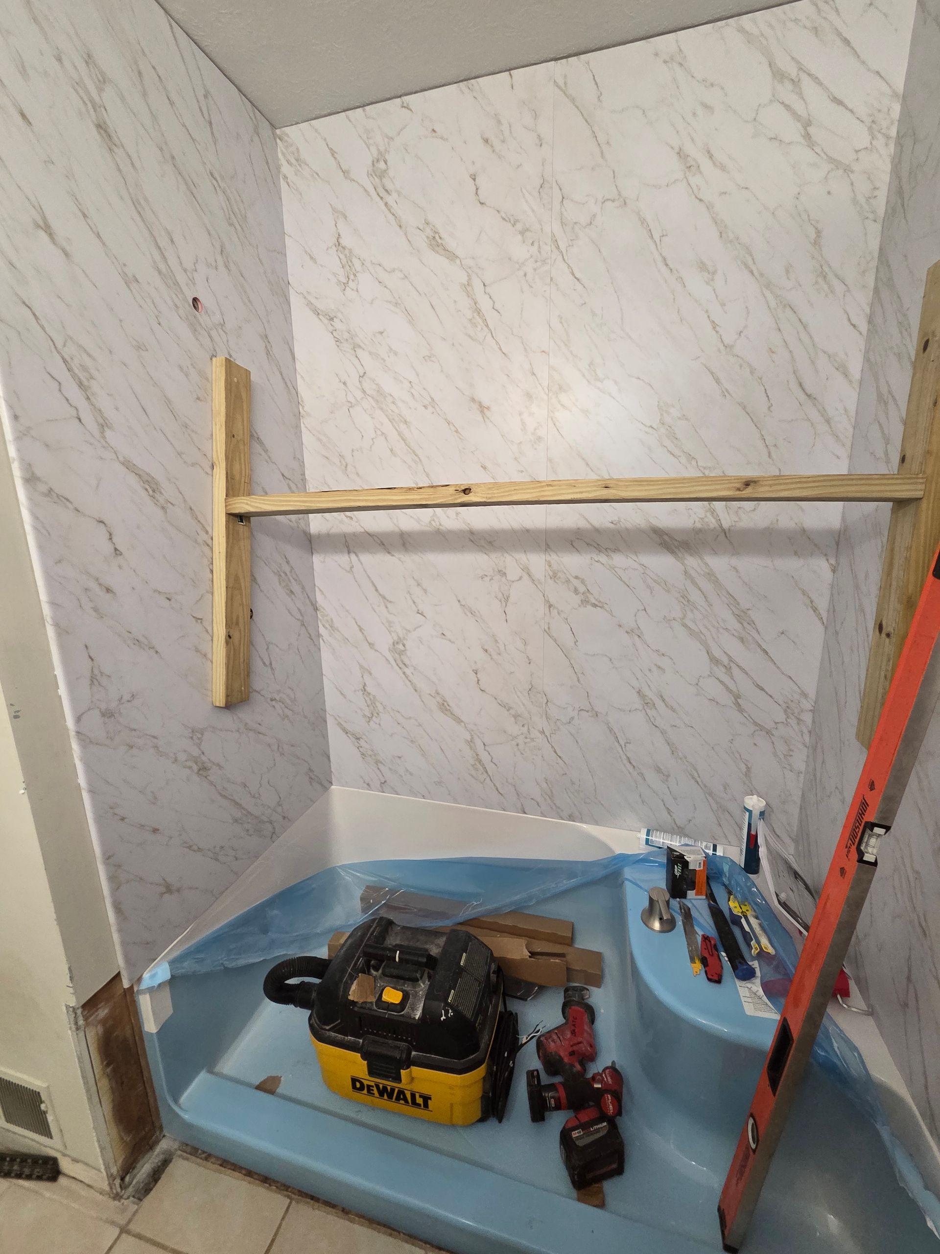 Small unfinished room with white walls, blue floor covering, tools, and a wooden support frame.