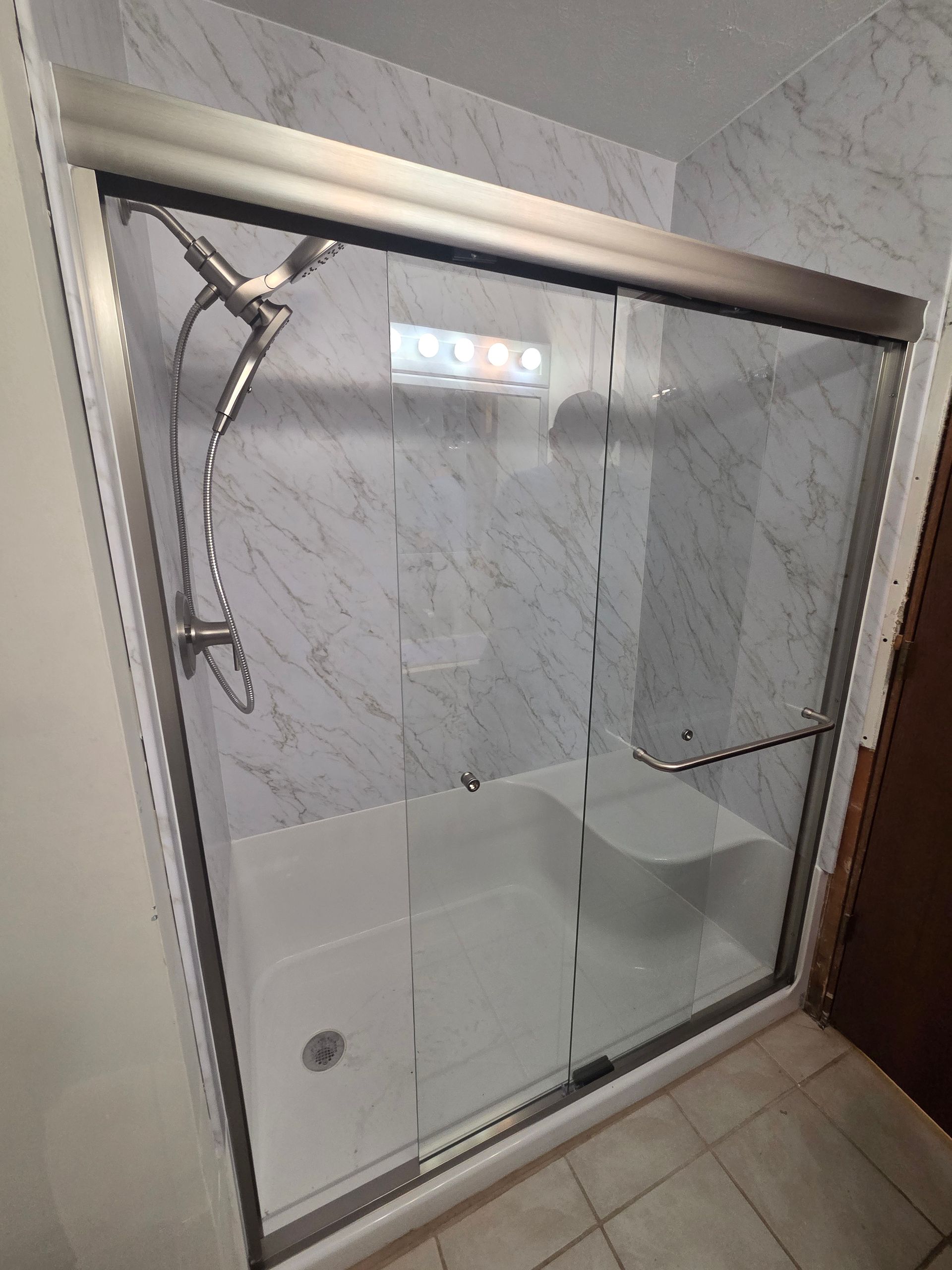 Clear glass shower enclosure with chrome frame, tiled walls, and a built-in bench.