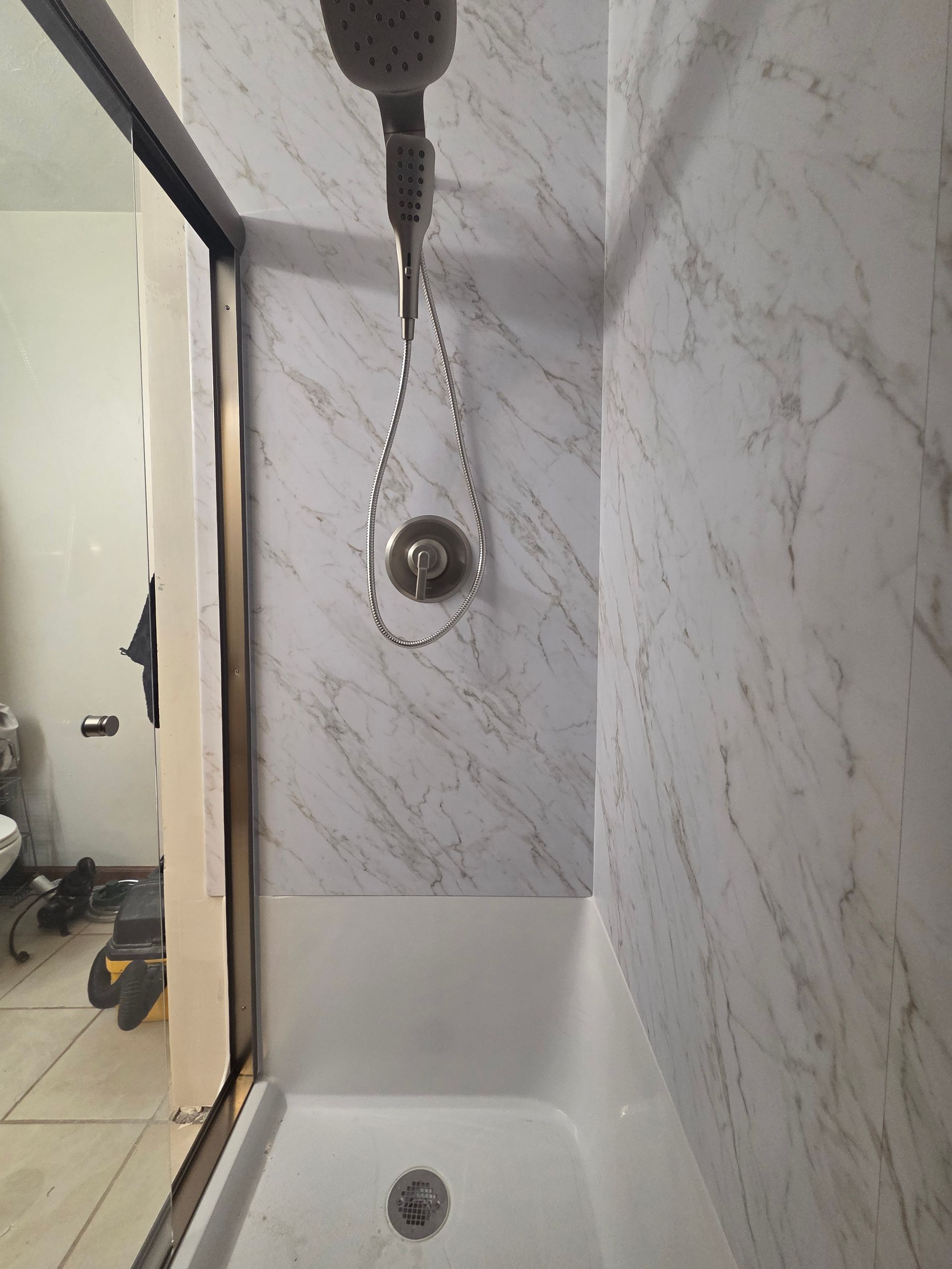 Shower stall with marble-look walls, built-in bench, and handheld showerhead.