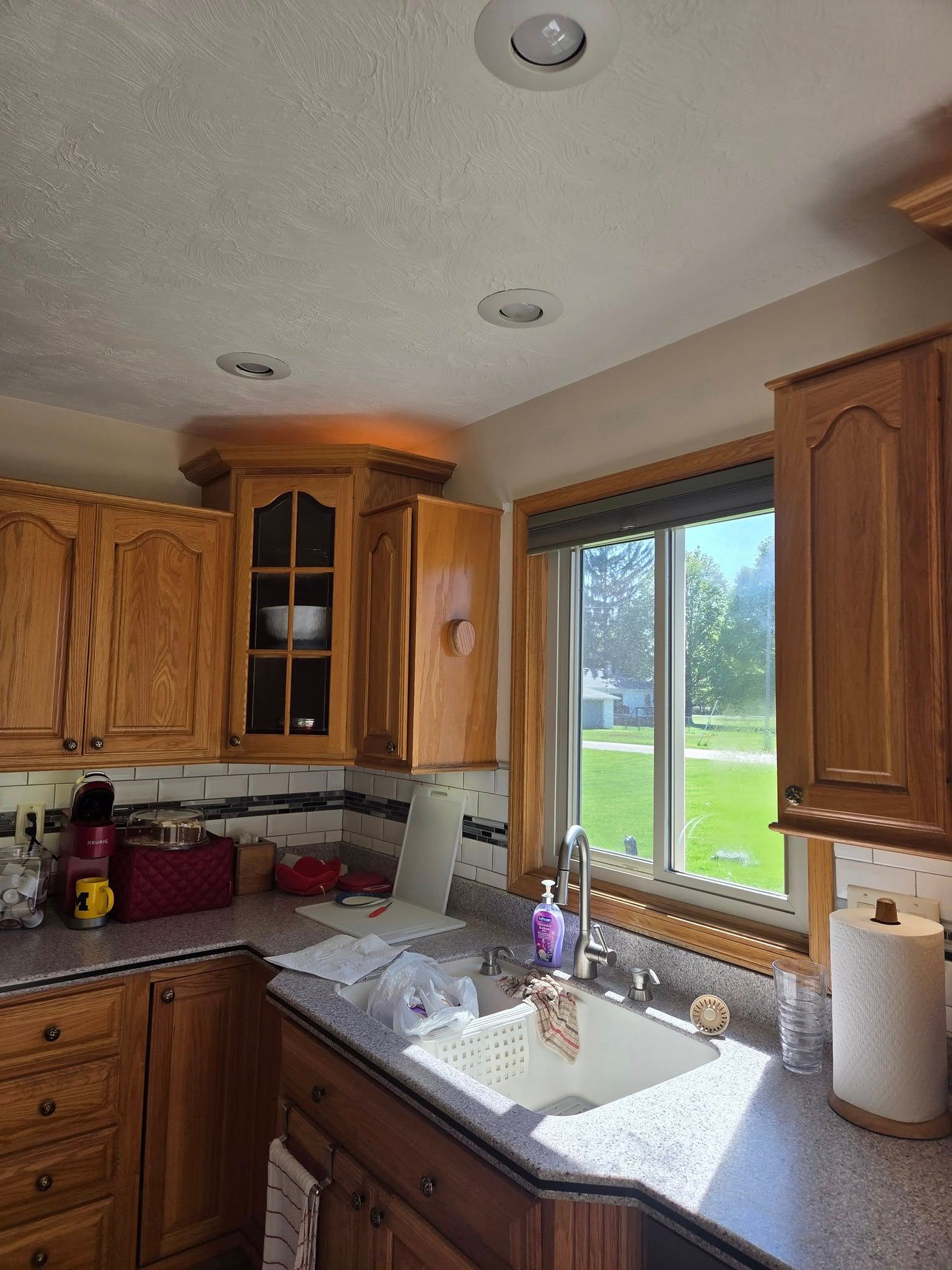 Sunlit kitchen with wood cabinets, granite counter, sink, and window overlooking a green yard