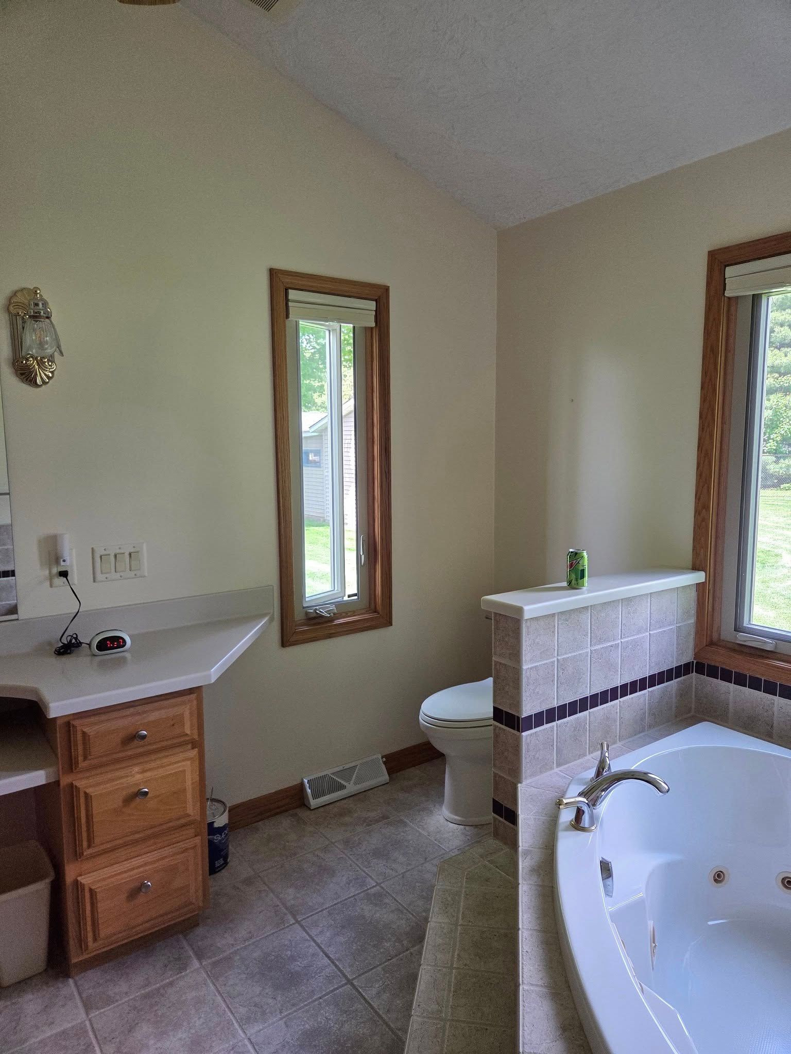 Bathroom with white tub, wood vanity, tiled floor, and two windows letting in natural light