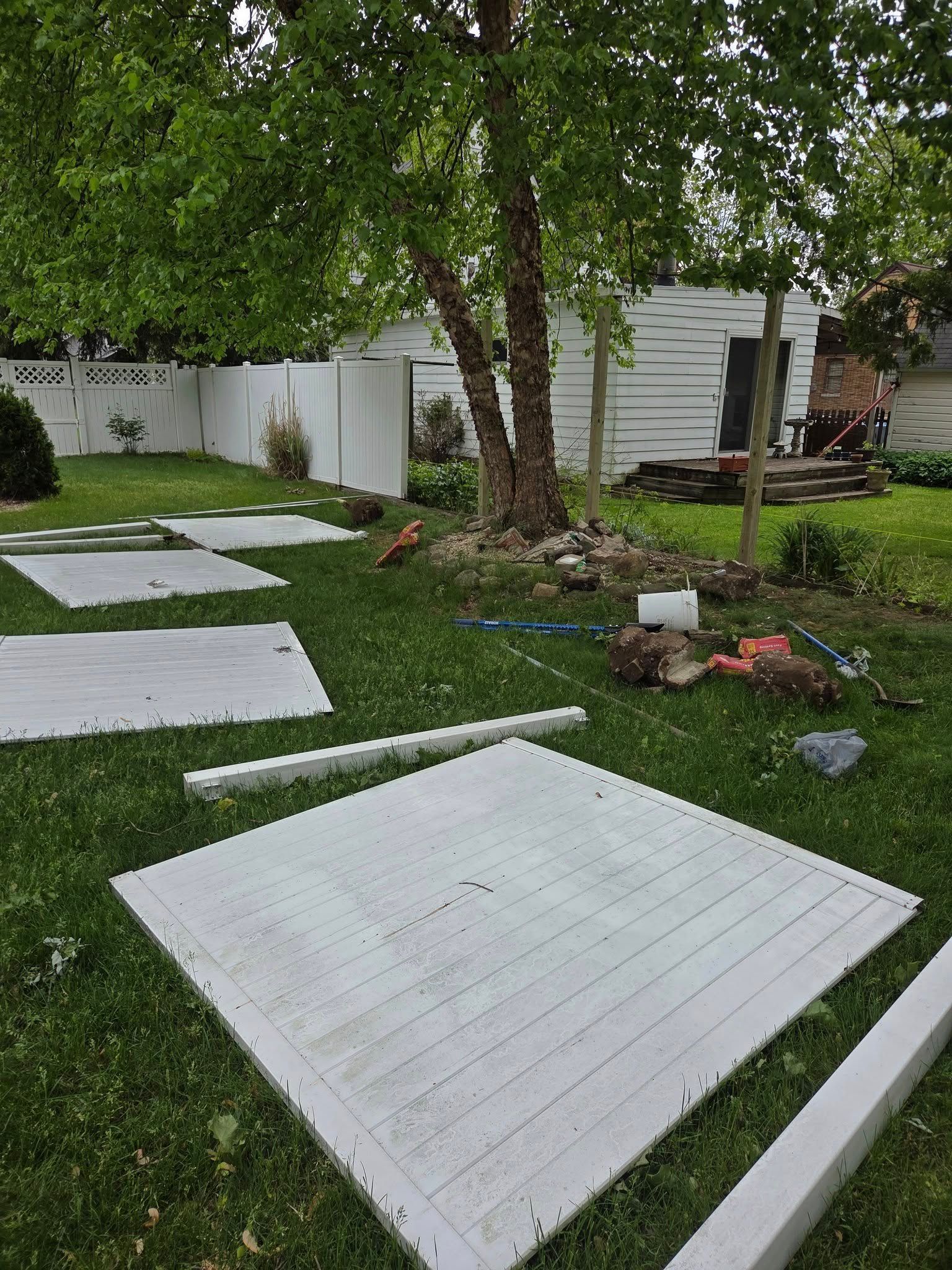 White stepping stones on a green lawn beside trees and a fenced yard