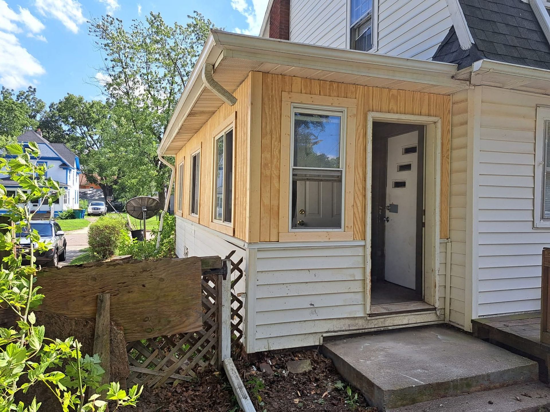 Small enclosed porch addition on a white house with wood trim and a front door by a concrete step.