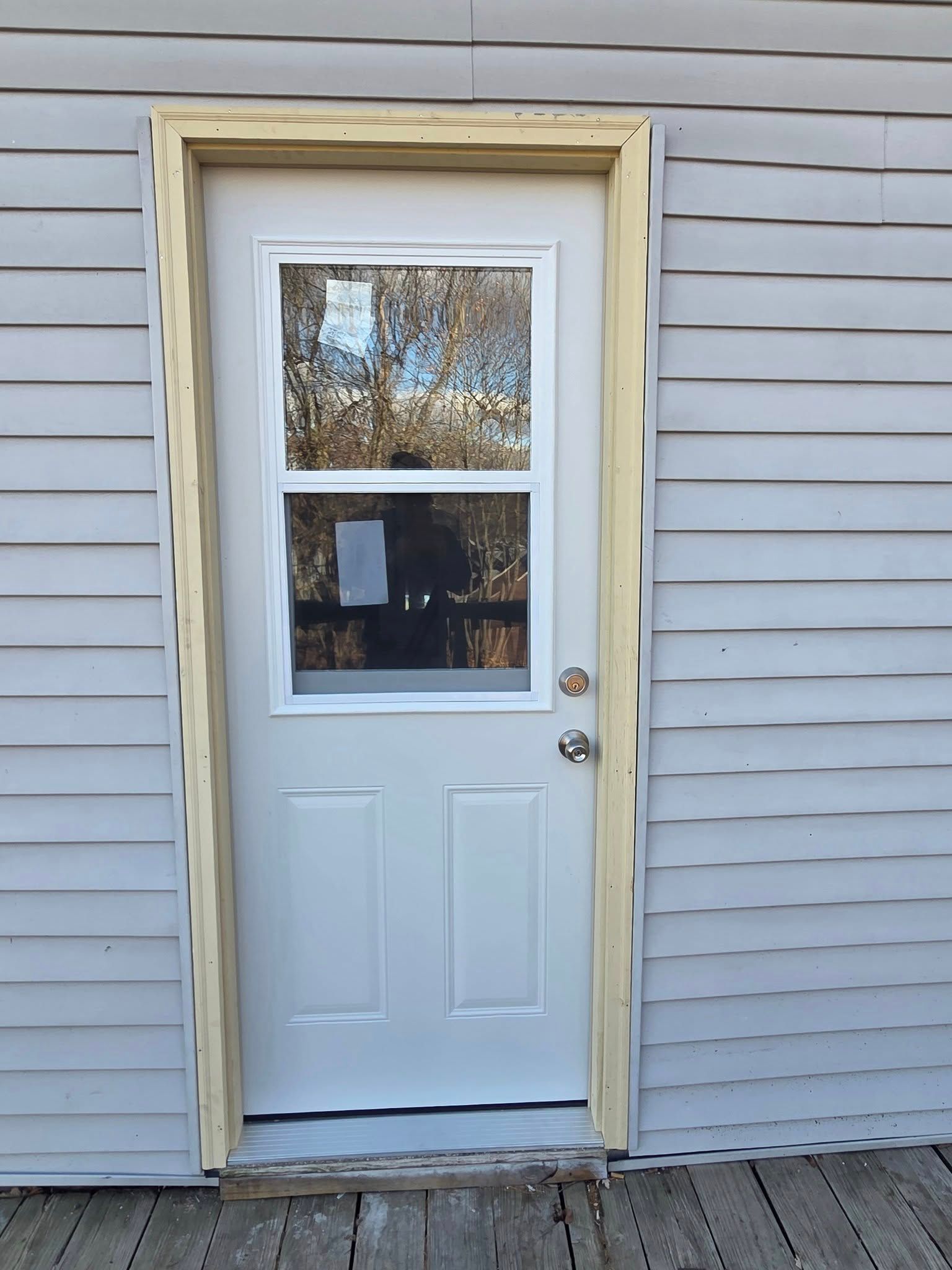White exterior door with window and yellow trim on a gray-sided house