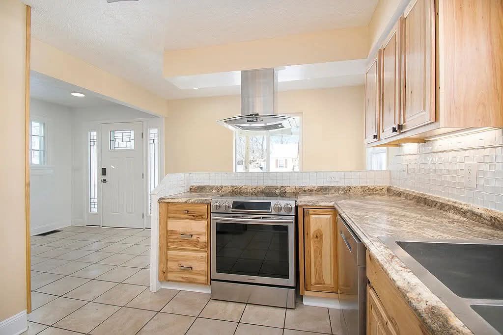 Bright kitchen with granite counters, wood cabinets, tiled floor, and white appliances near a sunlit entryway