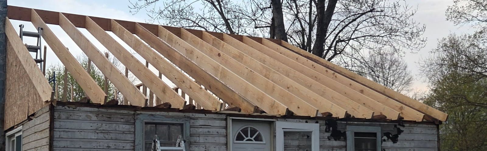 Roofless house under renovation with exposed wooden rafters and gray siding