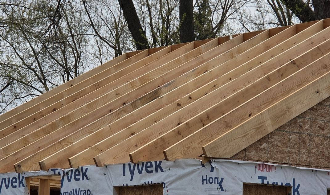 Wood-framed roof under construction with exposed rafters and house wrap along the eaves