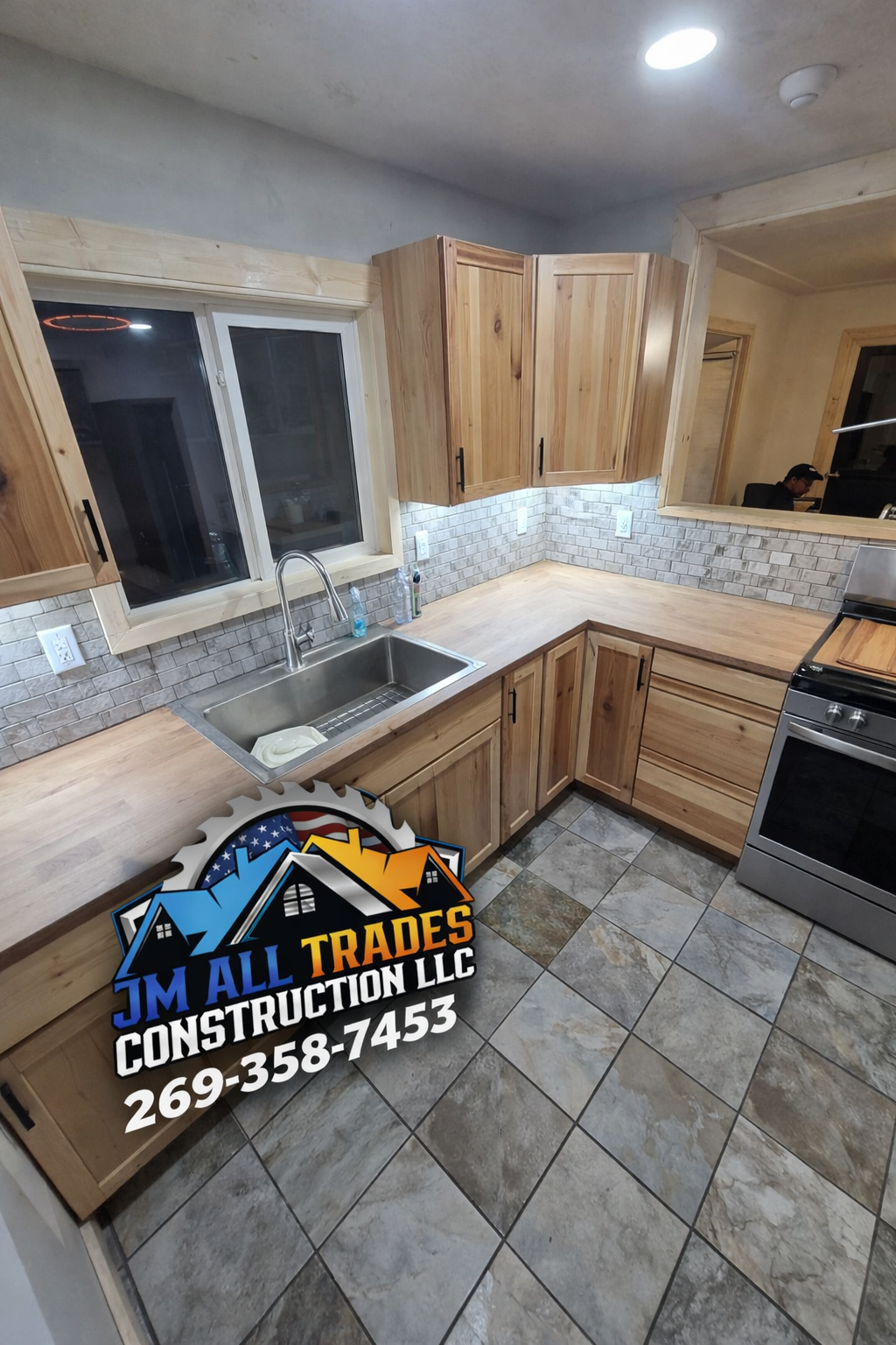 Kitchen with wood cabinets, tiled backsplash, window, stainless sink, and visible contractor sign on the floor.