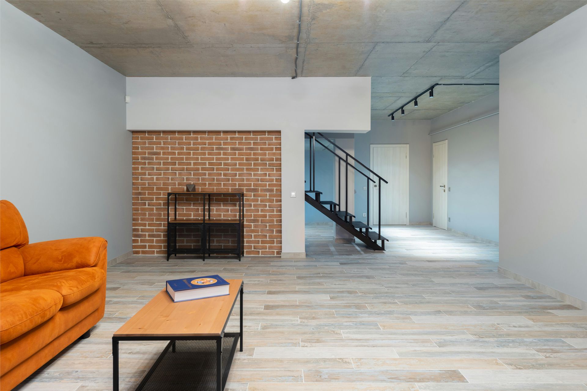 Modern living room with orange sofa, coffee table, brick fireplace, and staircase to upper floor